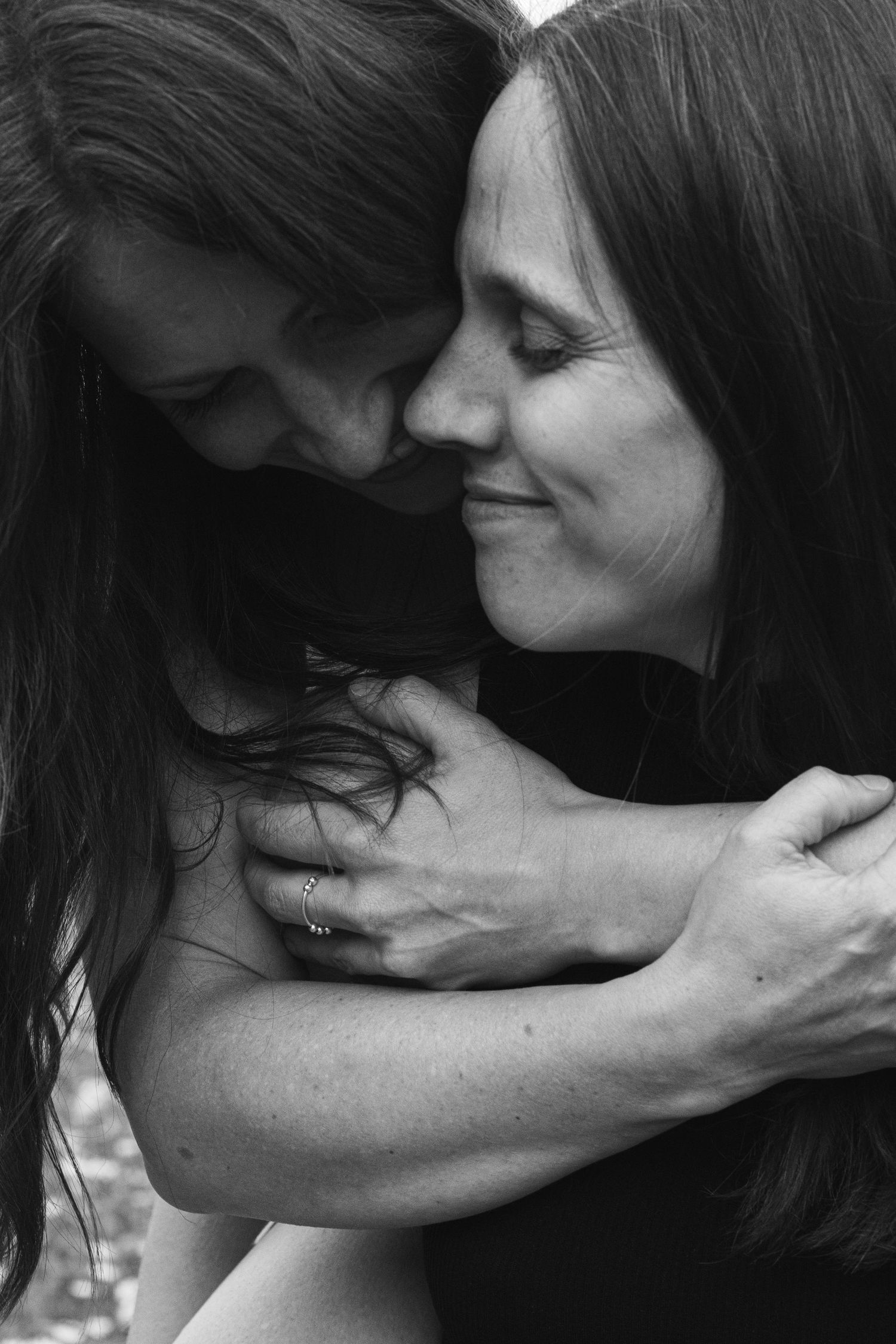 Two women share a tender embrace in a black and white portrait, smiling with eyes closed.