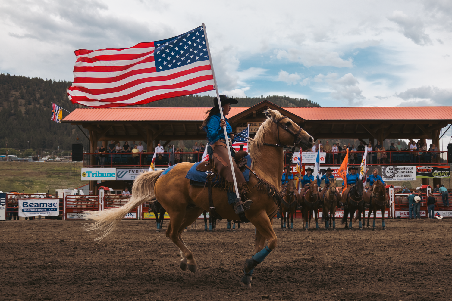 Equestrian carries a large American flag on a galloping horse during a rodeo grand entry.