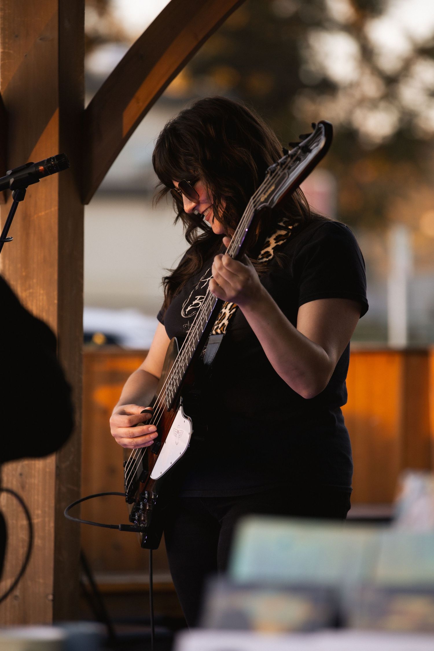 Female guitarist with dark hair performs passionately on electric bass guitar at an outdoor evening concert.