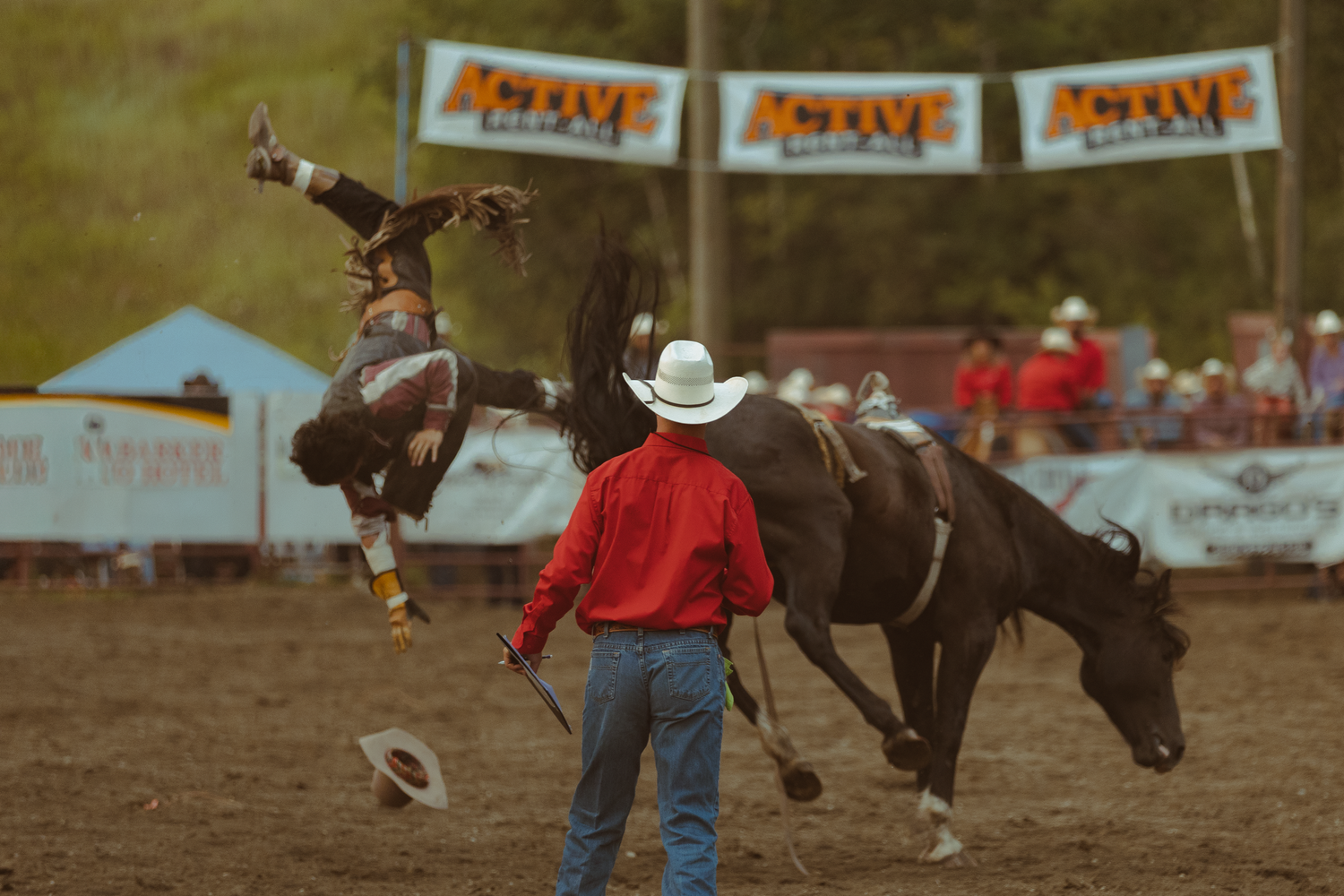 A rodeo rider gets bucked off a horse at an outdoor rodeo event with Active banners in the background.