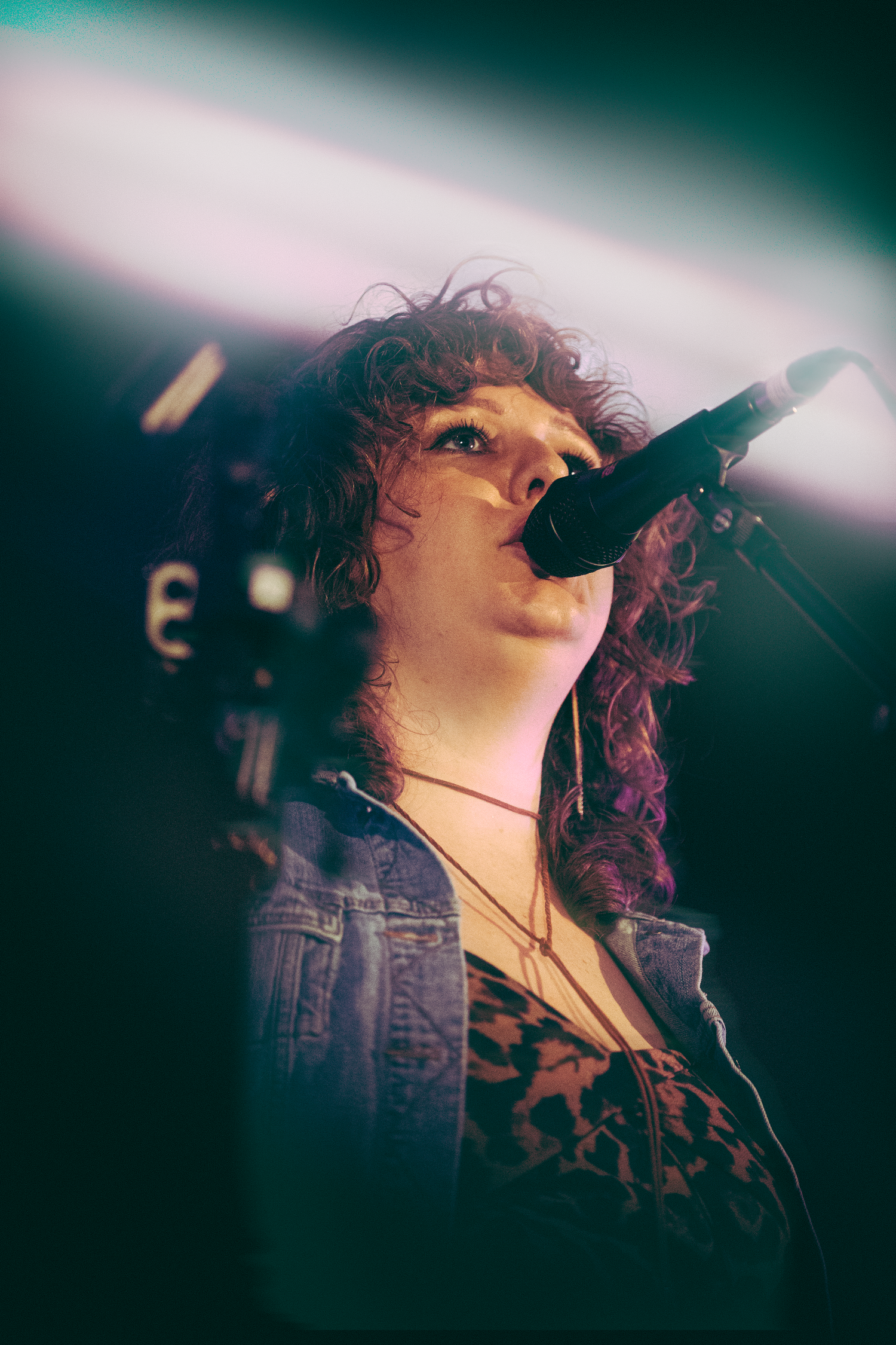 Young female vocalist singing into microphone on stage, illuminated by dramatic beam of light during live concert.