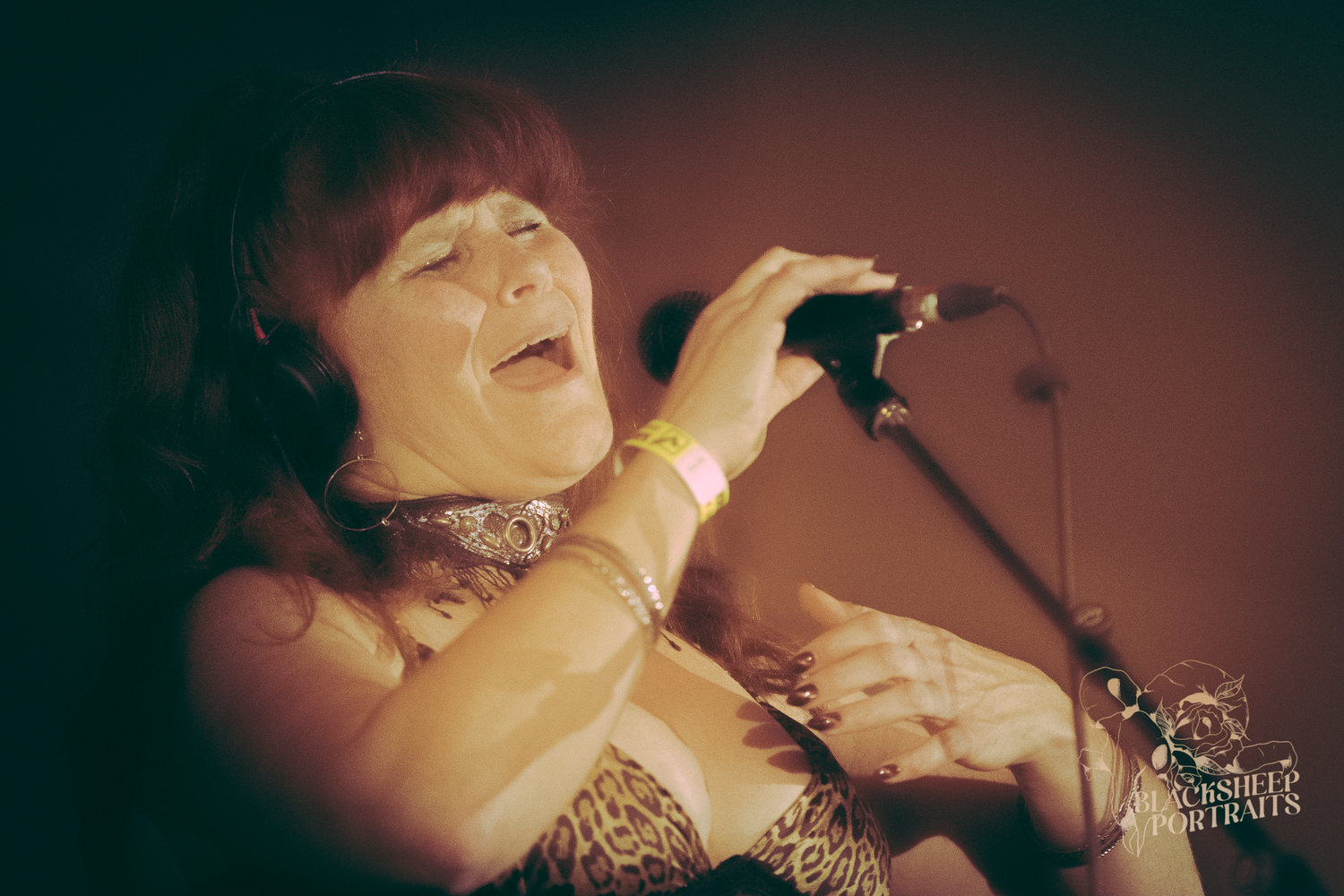 Woman singer passionately performing live on stage, gripping microphone with eyes closed under warm stage lighting.