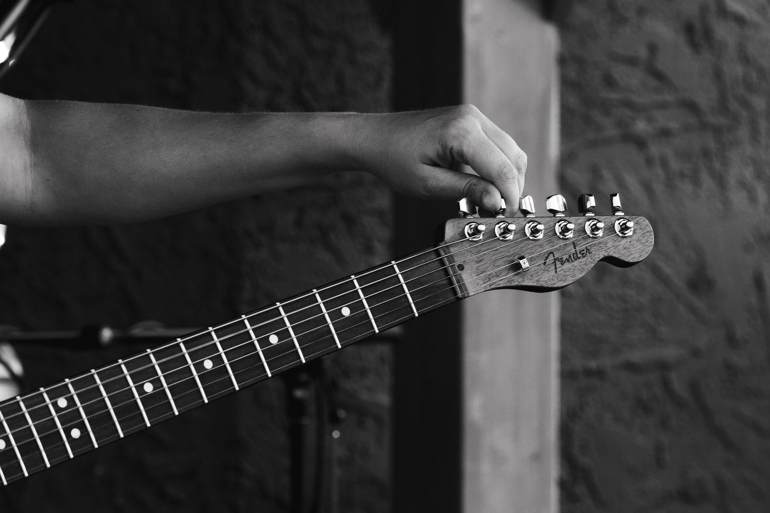 Black and white close-up of hands on a Fender guitar neck during a live performance.