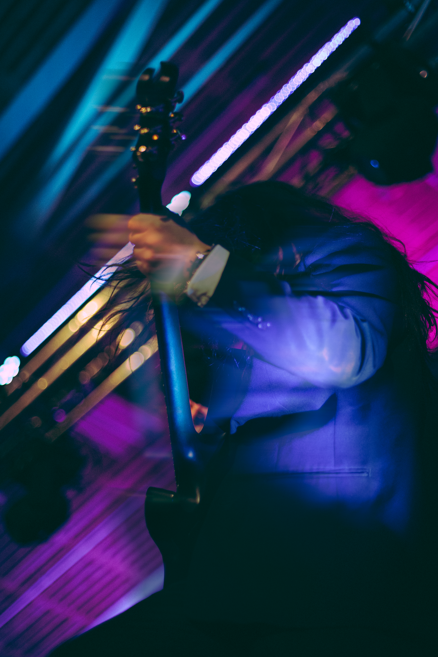 Dynamic motion-blur shot of guitarist performing on stage under vibrant purple and blue concert lighting.