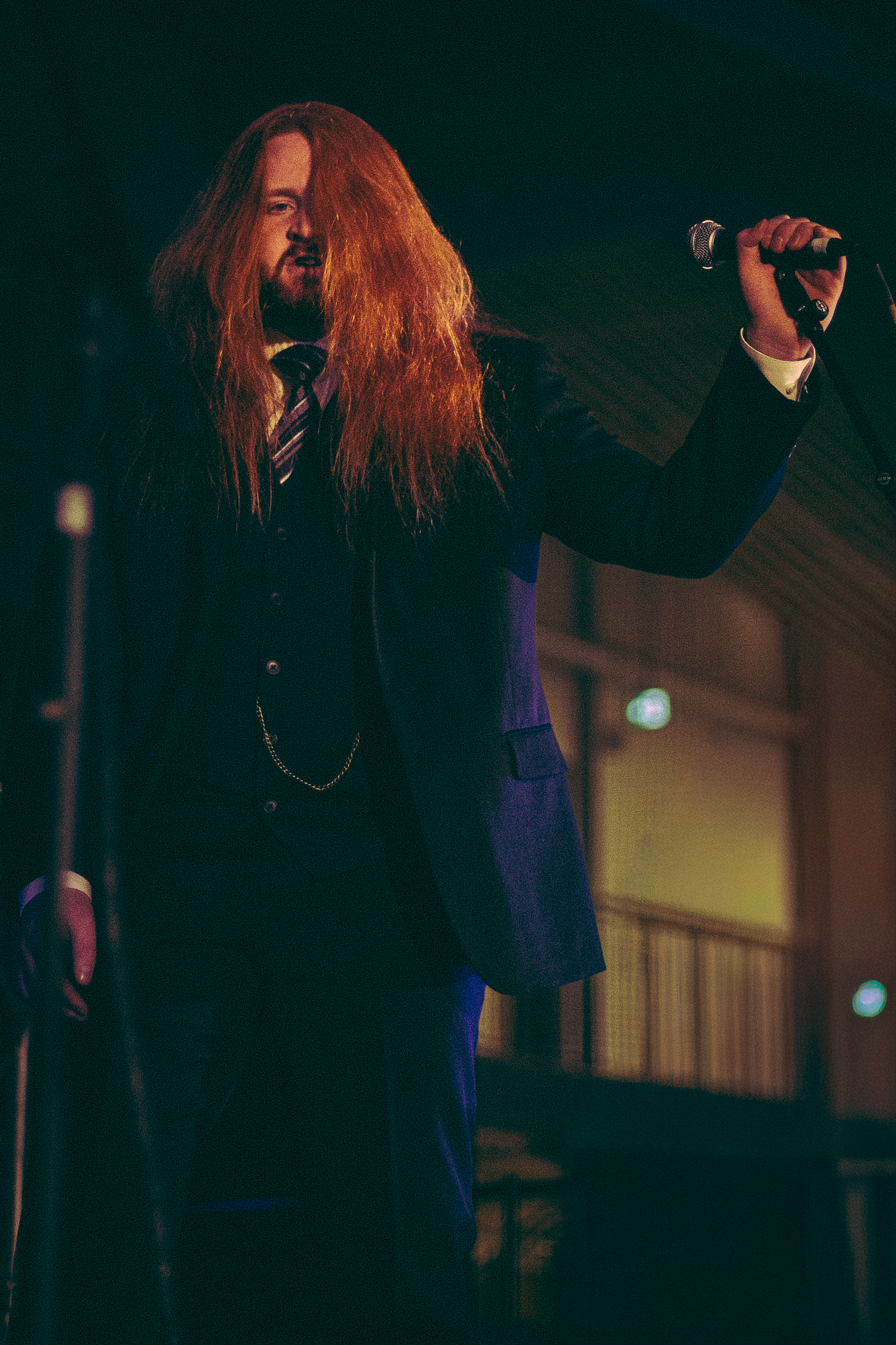 Red-haired male singer holding microphone aloft while performing live on stage in a suit.