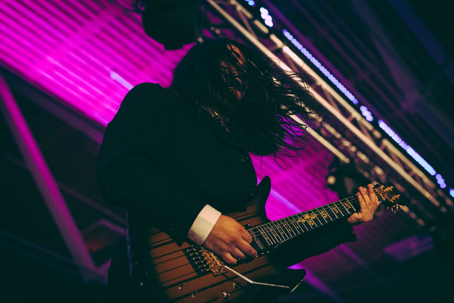 Electric guitarist with flying hair performing under purple stage lights at a live concert.