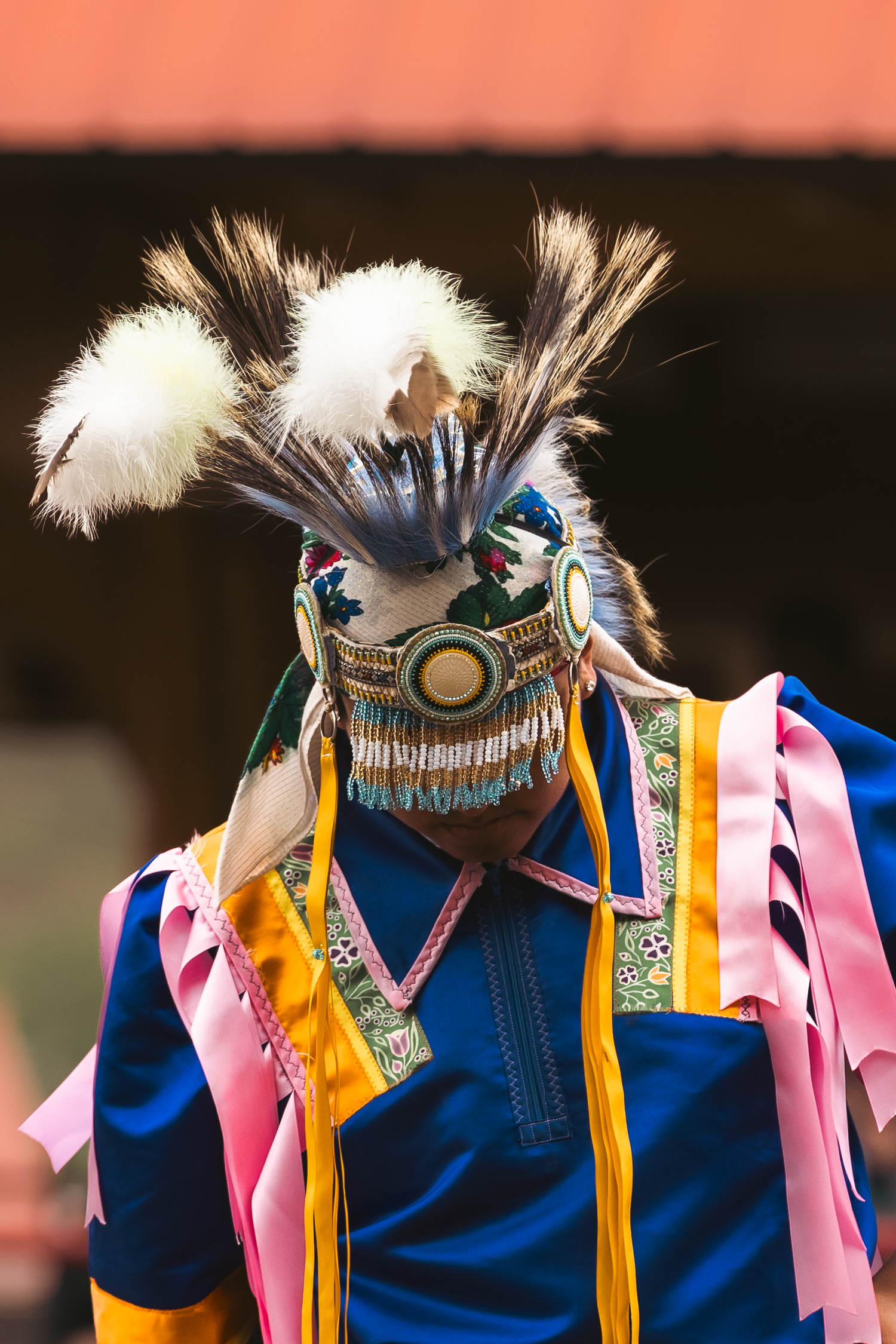 Close-up of a performer in colorful Indigenous regalia with elaborate feathered headdress at a cultural event.