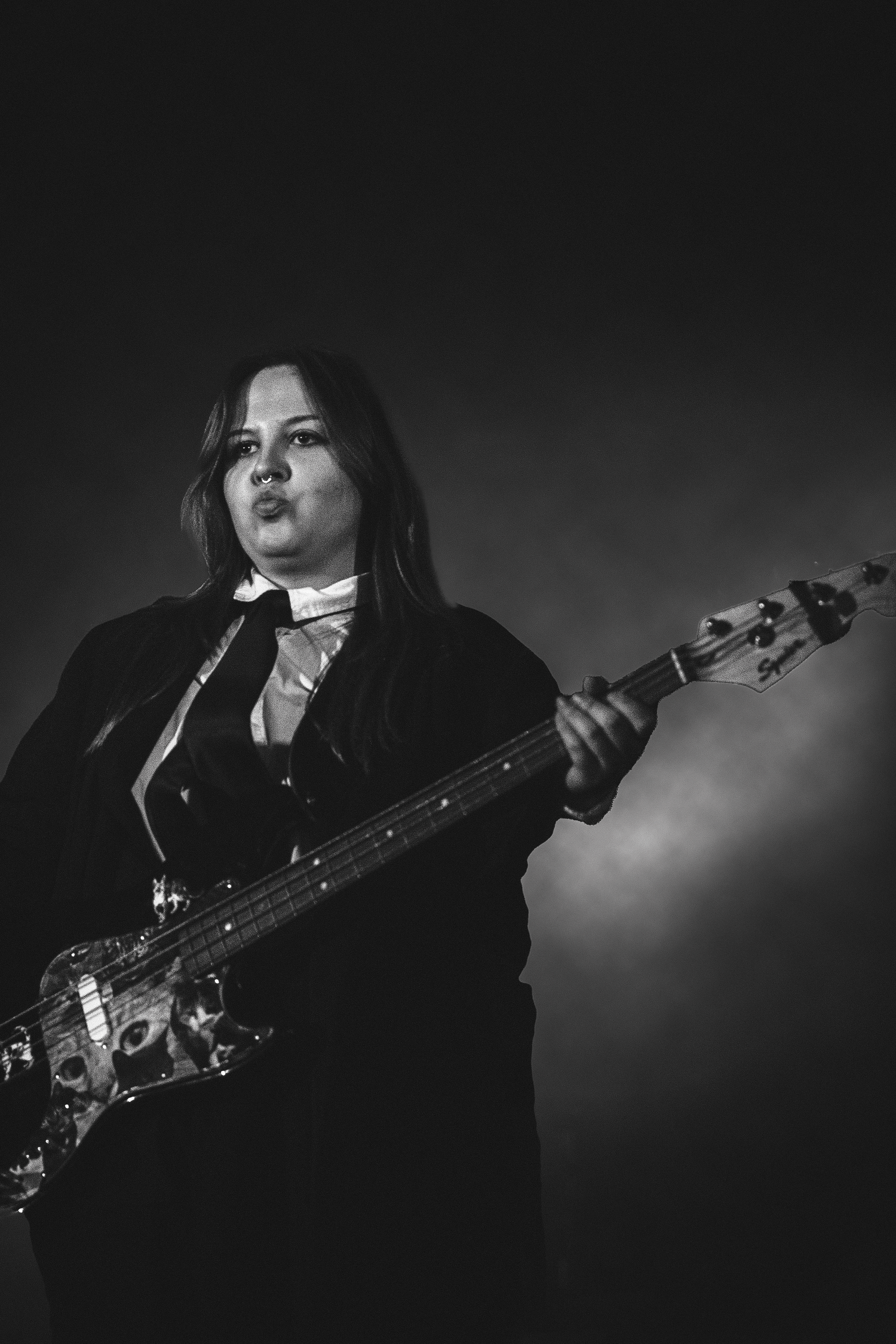 Black and white photo of a female bassist playing electric guitar on stage during a live show.