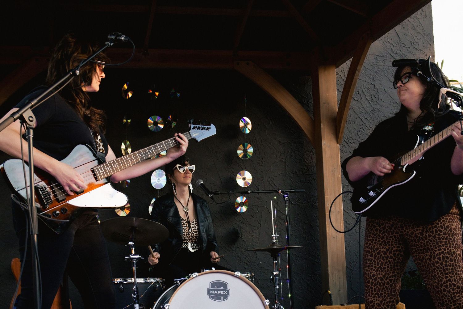 All-female rock band performing on outdoor stage with guitars and drums in natural light.