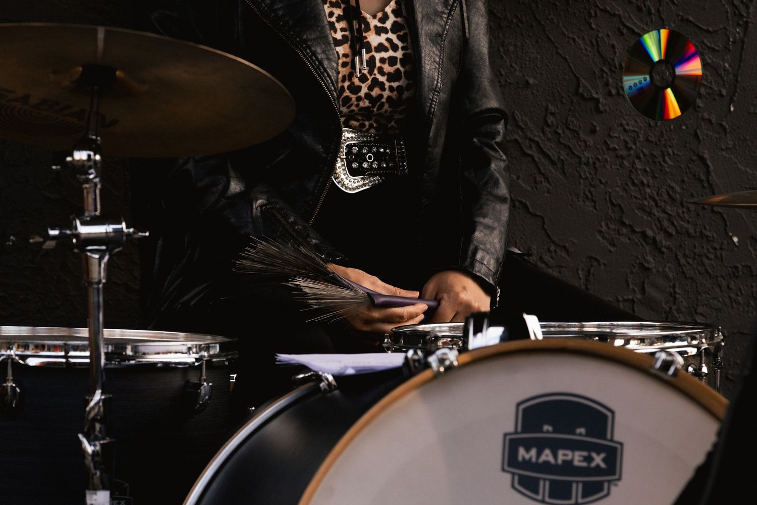 Close-up of female drummer in leopard print playing Mapex bass drum with brush drumsticks.