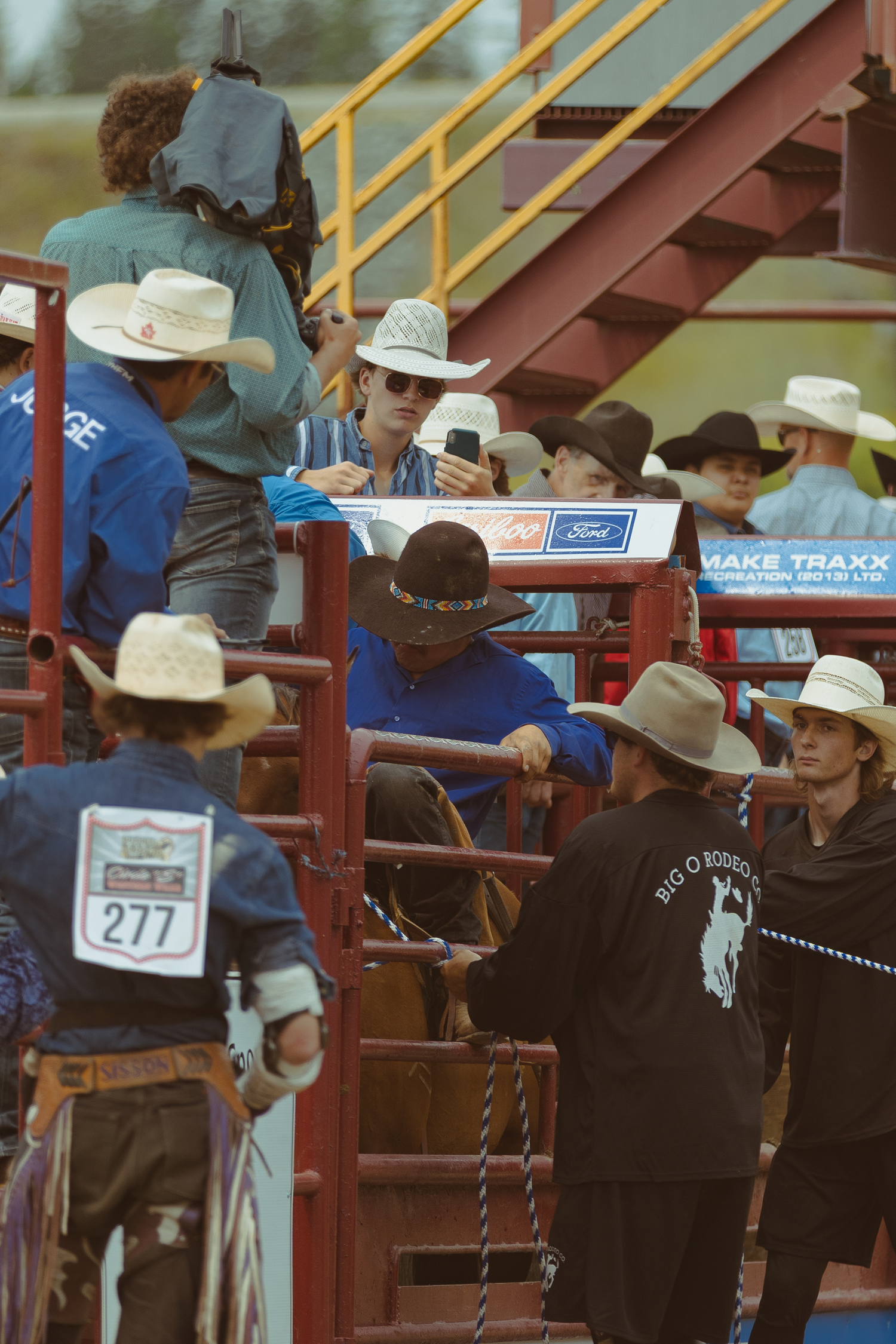 Cowboys in white hats gather near the red metal chutes at a rodeo, with number 277 visible.
