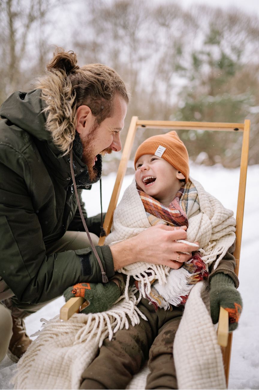 Familien Fotografie Papa und Kind lachen im Schnee auf dem Schlitten