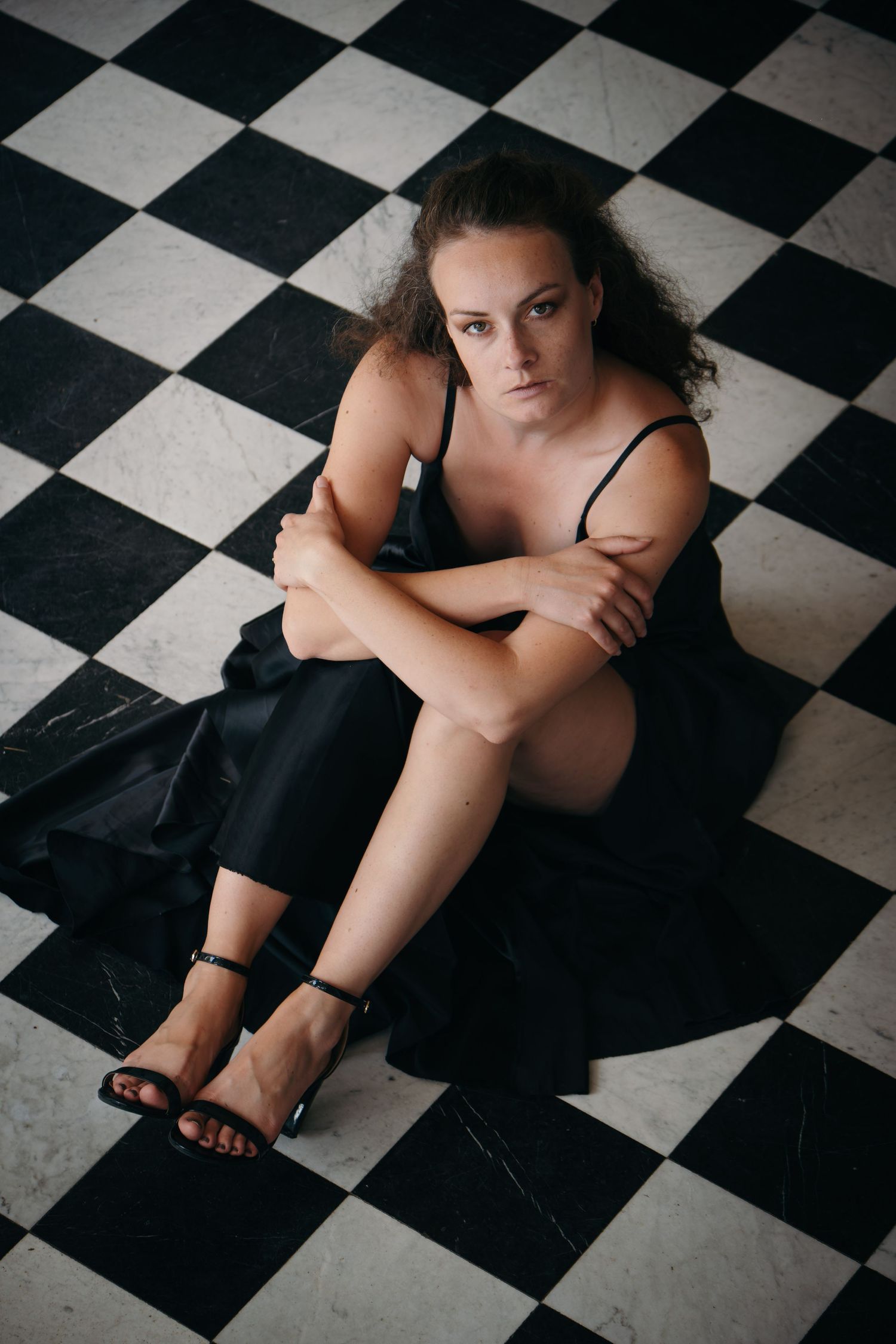 Portrait d'une jeune femme assise sur un sol à damier dans une lumière douce.