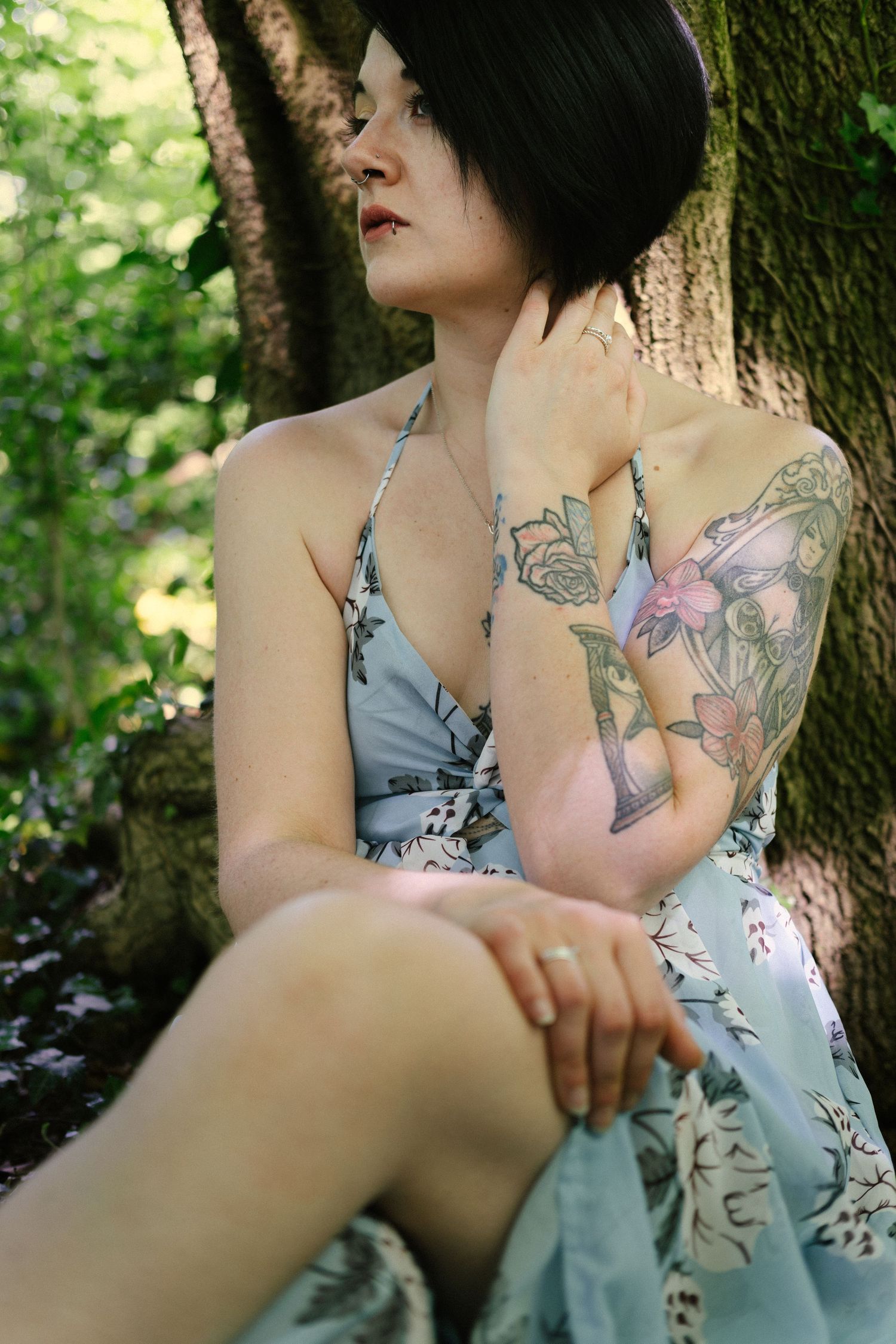 Portrait d'une jeune femme tatouée assise contre un arbre en lumière naturelle.