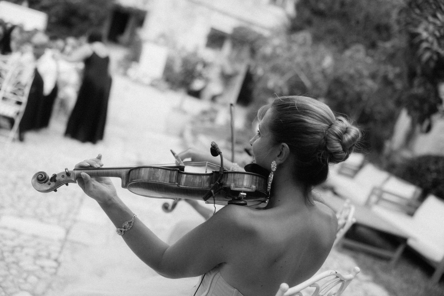 Elegant violinist performing at an outdoor wedding reception in black and white.