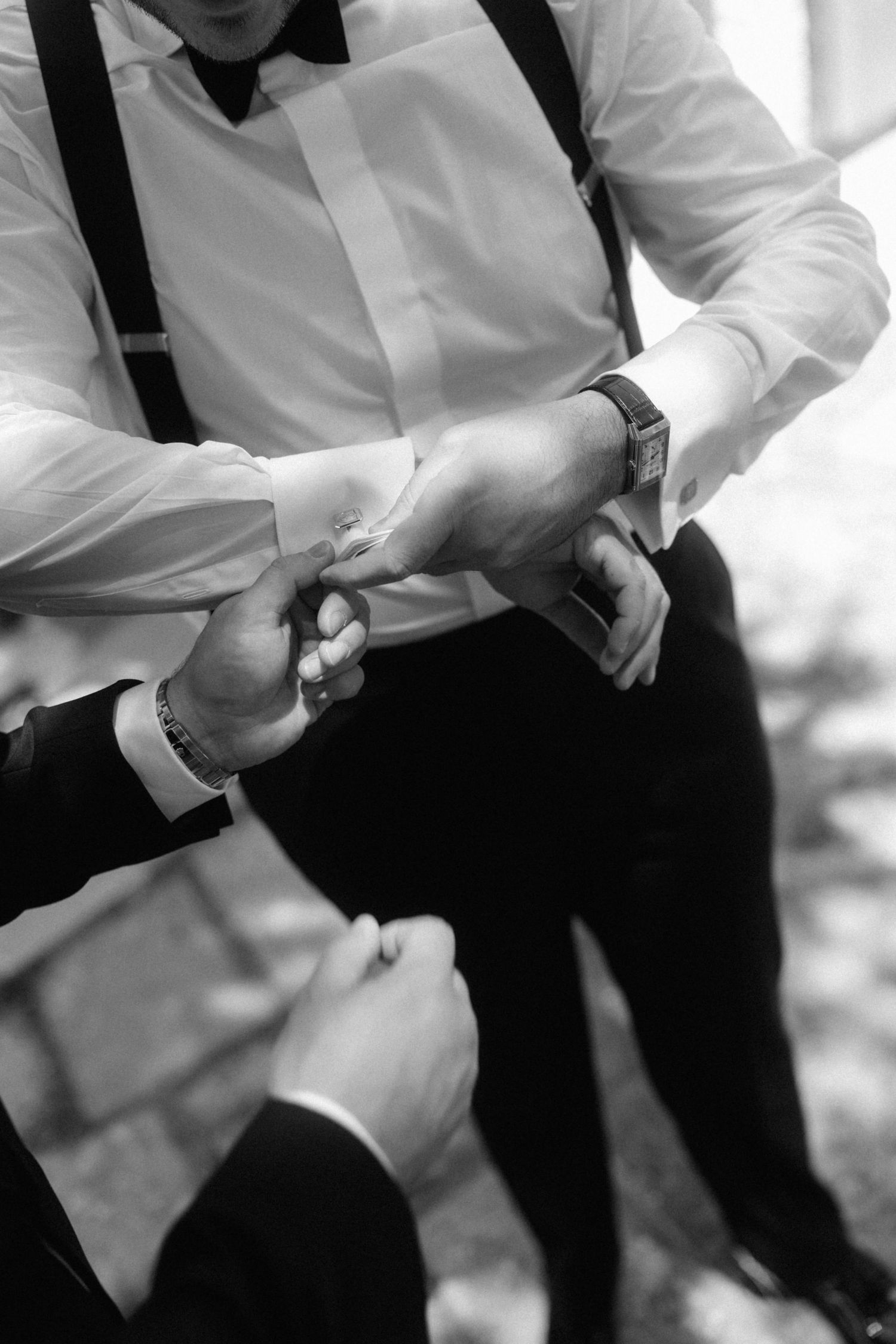 Black and white close-up of groomsmen helping adjust cufflinks before a wedding ceremony.