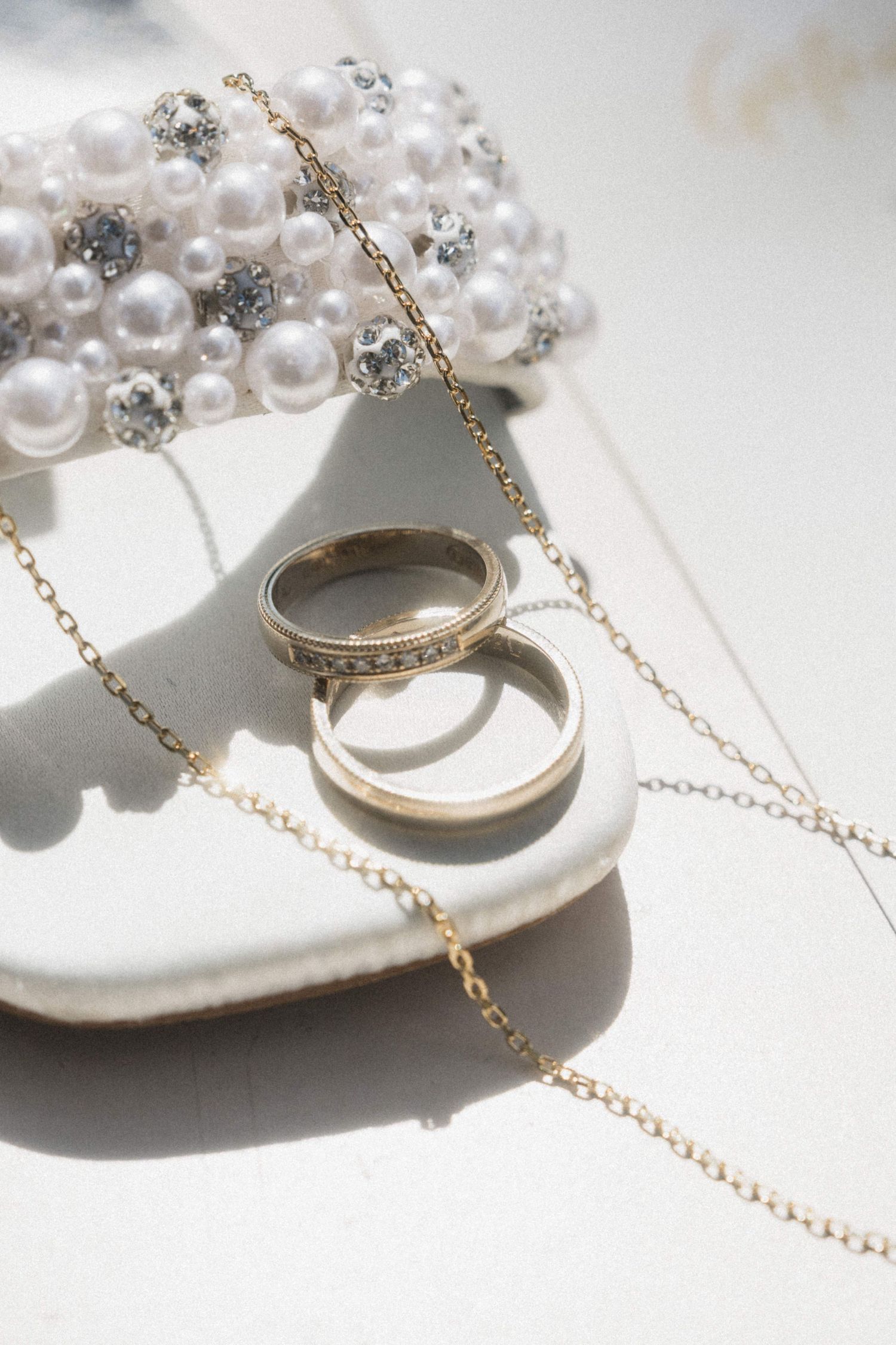 Two gold wedding bands resting on a pearl and crystal embellished bridal shoe with gold chain necklace.