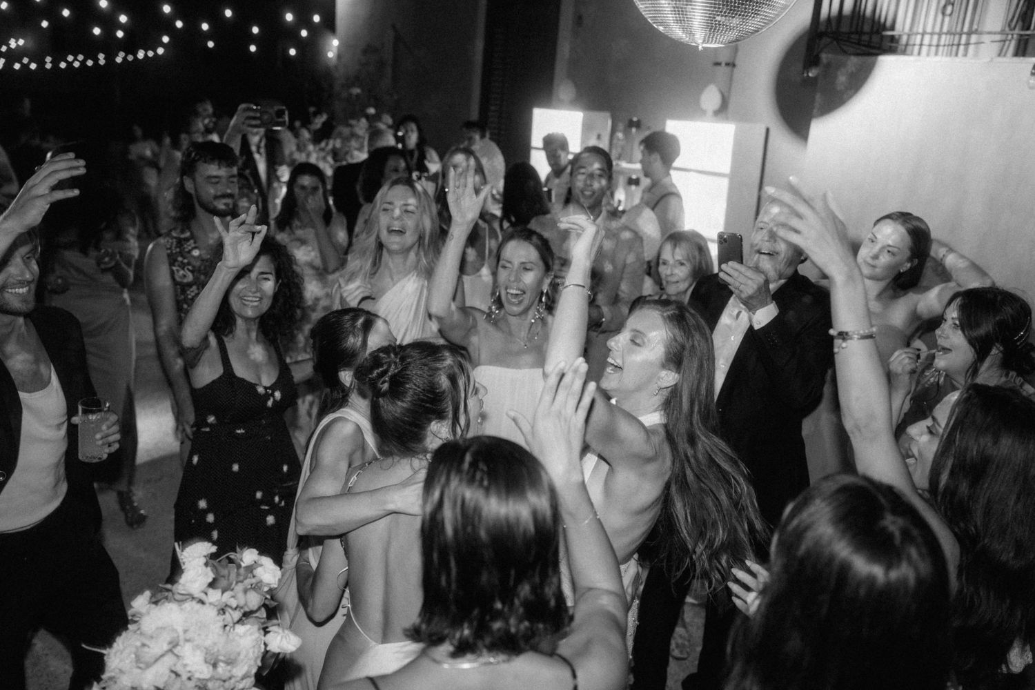 Black and white photo of wedding guests celebrating and dancing together on the dance floor.