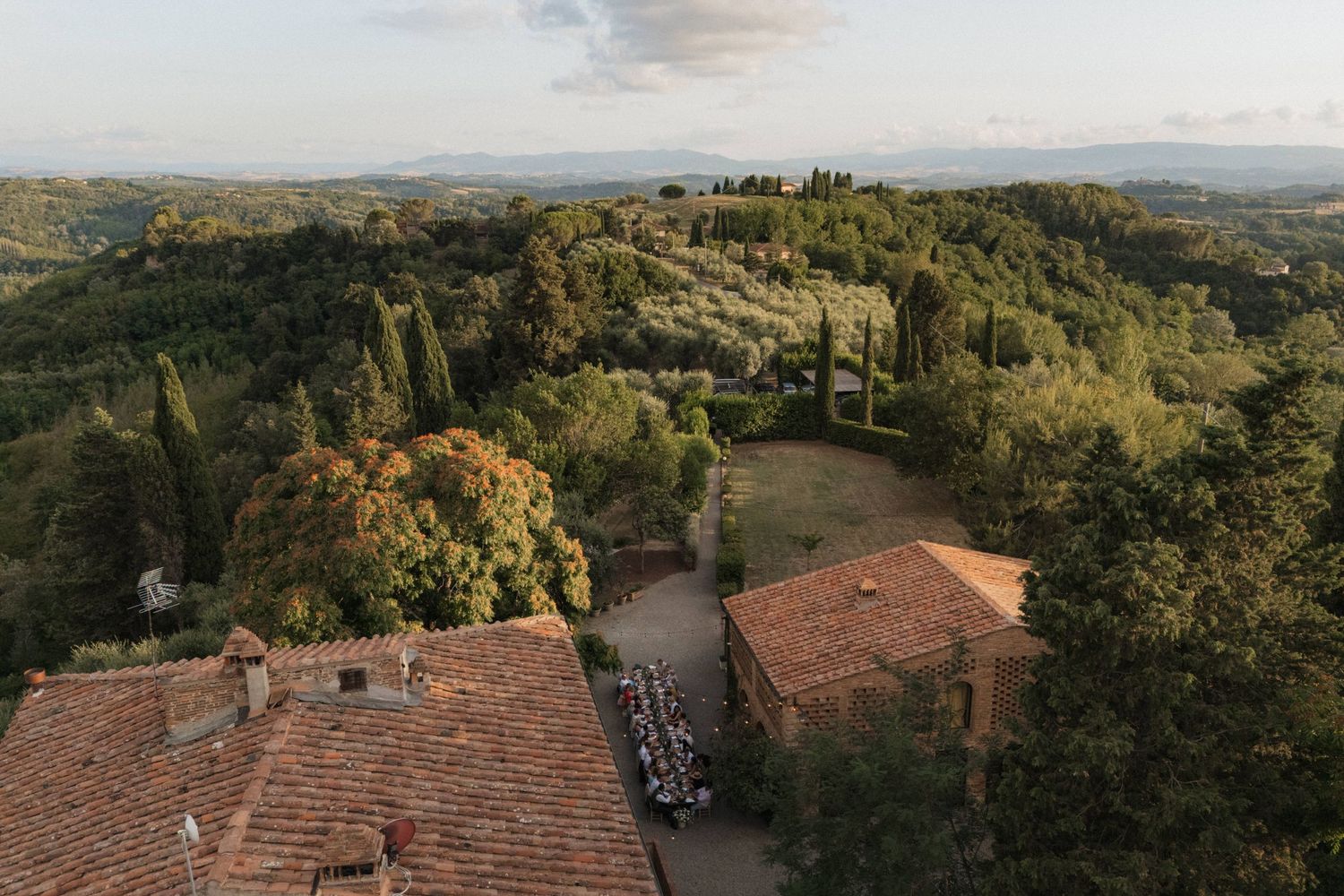 Aerial drone view of Tuscan countryside wedding venue with terracotta rooftops and rolling green hills.