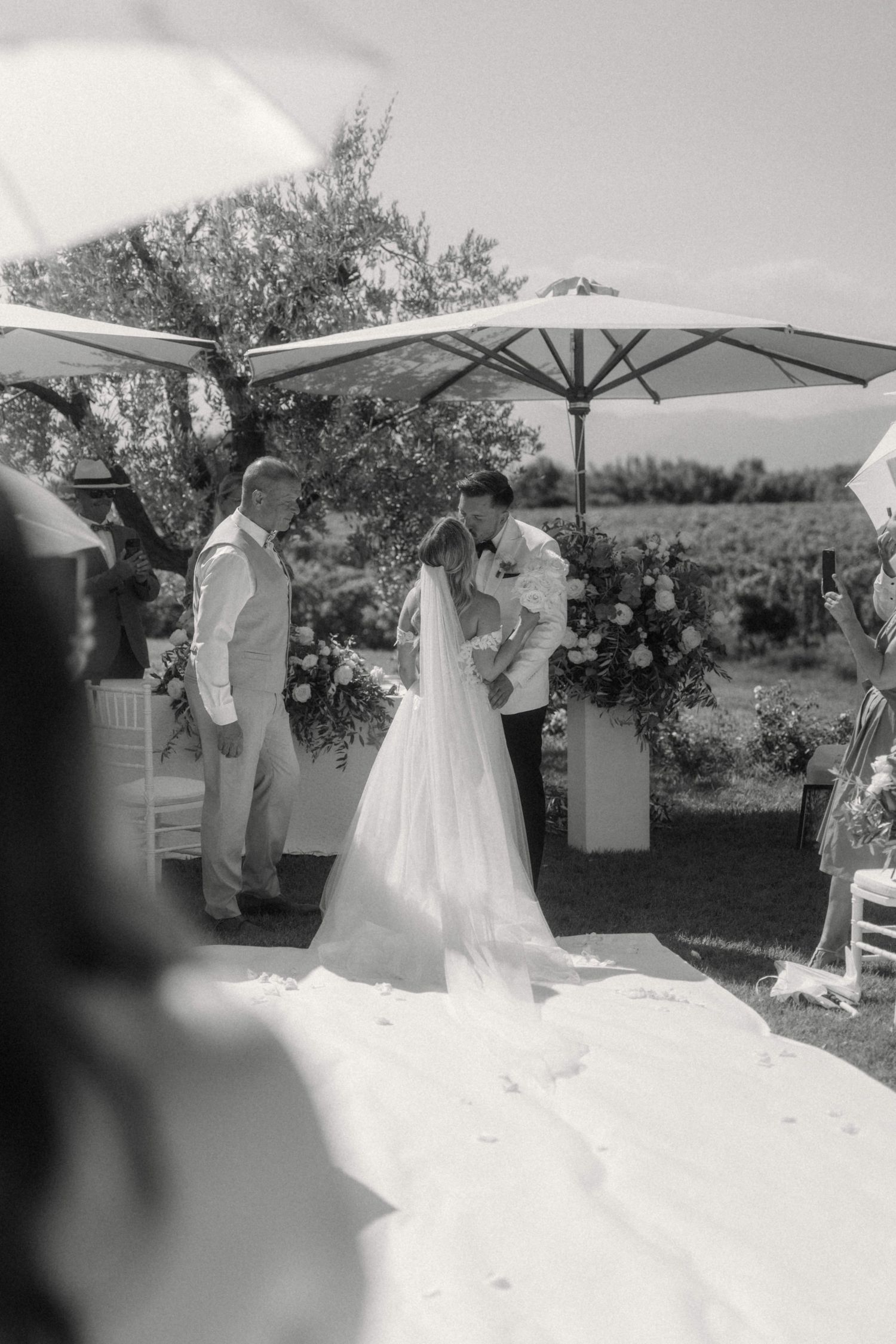 Black and white outdoor wedding ceremony with bride and groom under parasols.