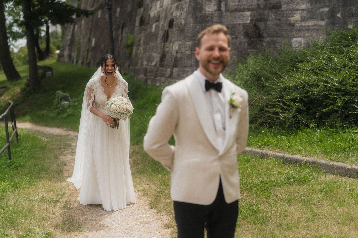 Groom in white tuxedo awaits first look as bride in lace gown approaches.