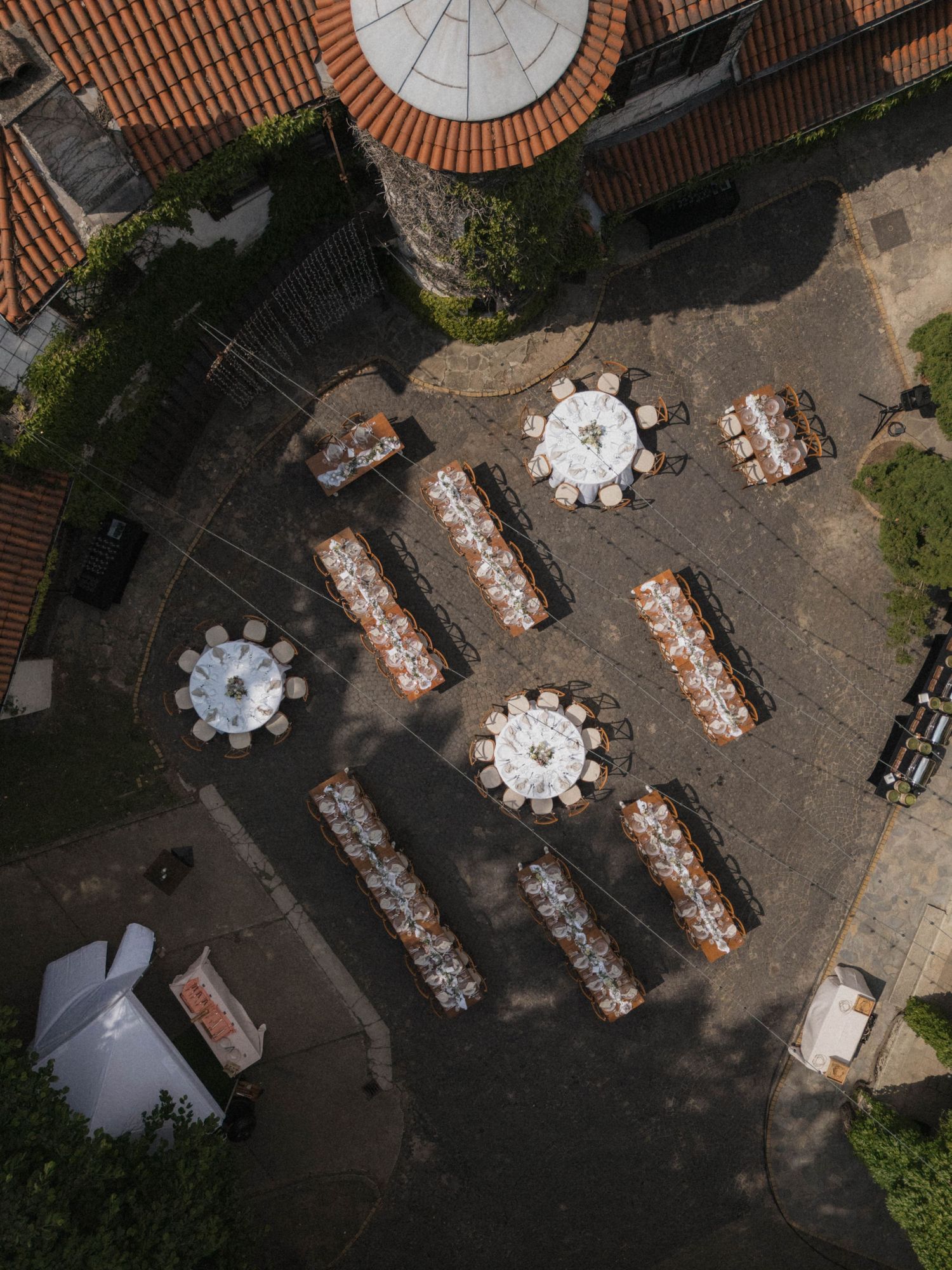 Aerial drone view of outdoor wedding reception tables arranged in courtyard of rustic stone estate.