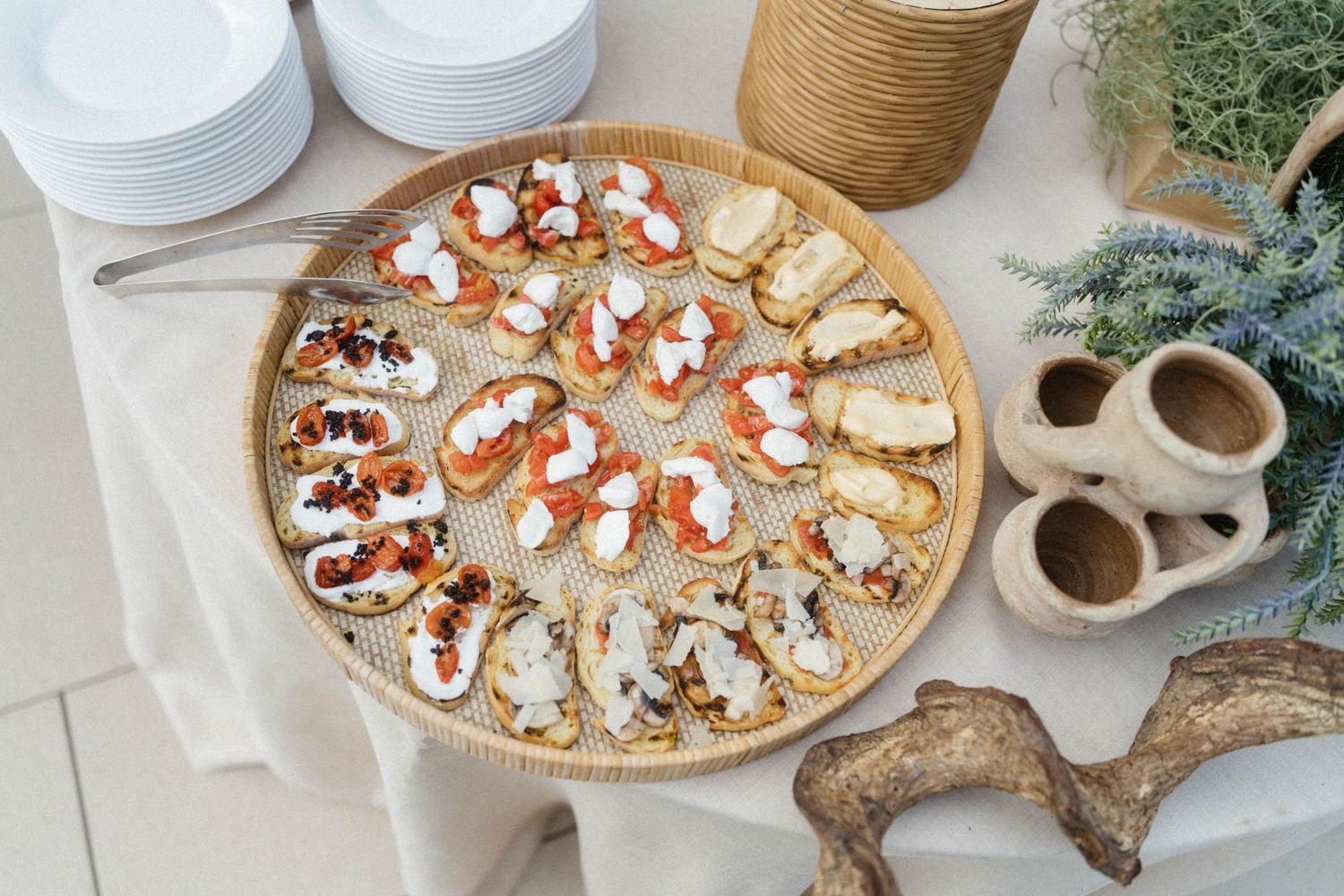 Elegant round wicker tray with assorted bruschetta topped with cream cheese, smoked salmon, and roasted vegetables.