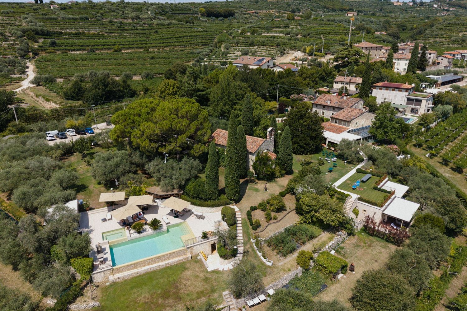 Aerial view of a Mediterranean villa with a swimming pool surrounded by lush gardens, olive trees, and vineyards.
