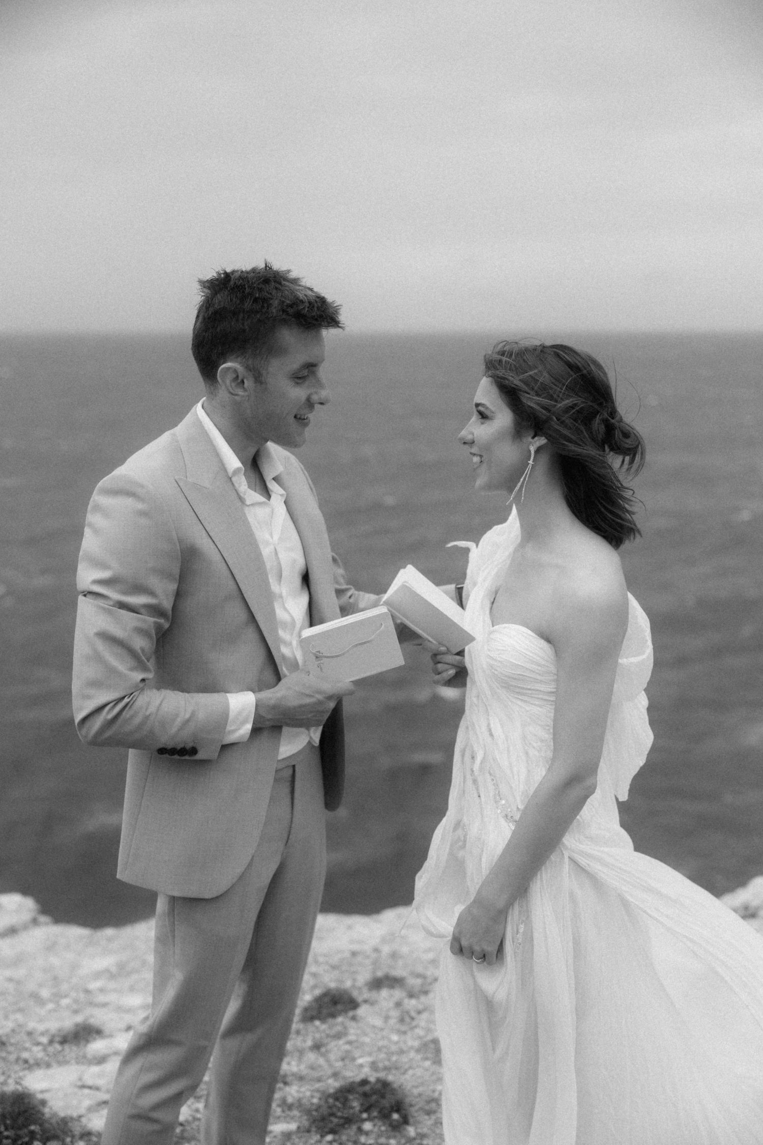 Black and white photo of a couple exchanging wedding vows on a cliff overlooking the ocean.