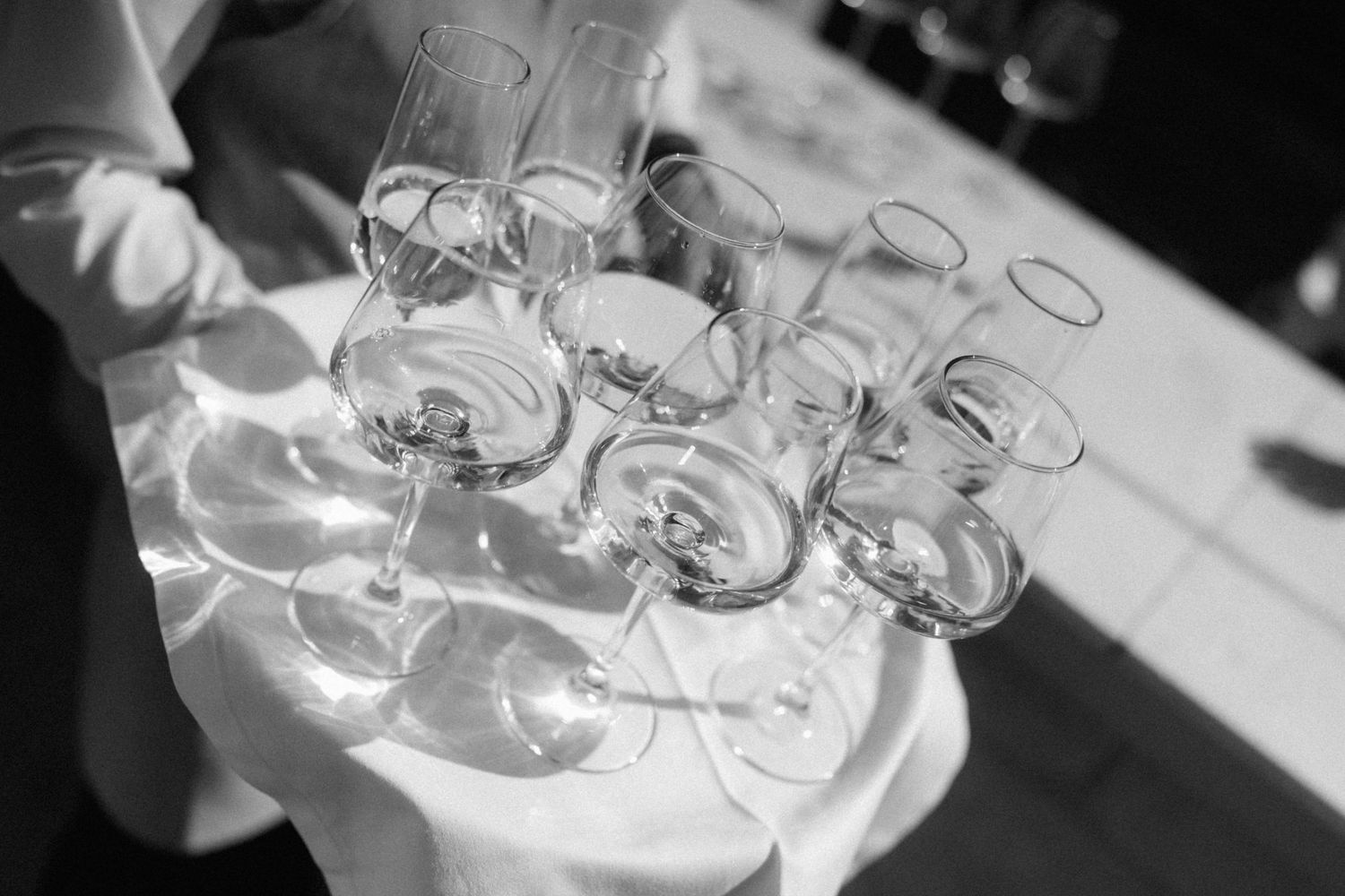 Black and white photo of a waiter holding a tray of empty wine glasses at a formal event.