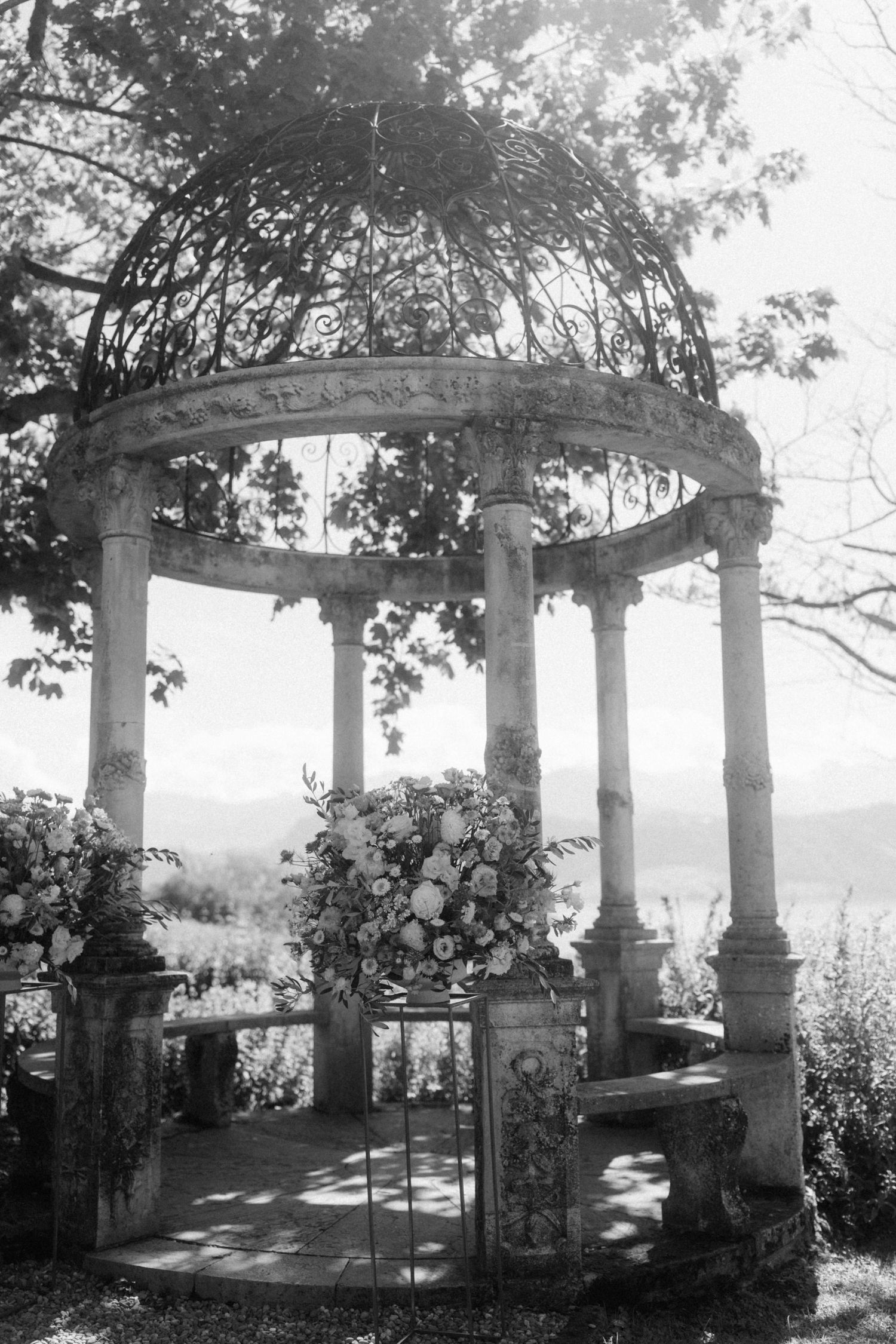 Elegant stone gazebo with ornate ironwork dome and floral arrangements overlooking scenic mountains, perfect wedding ceremony backdrop.