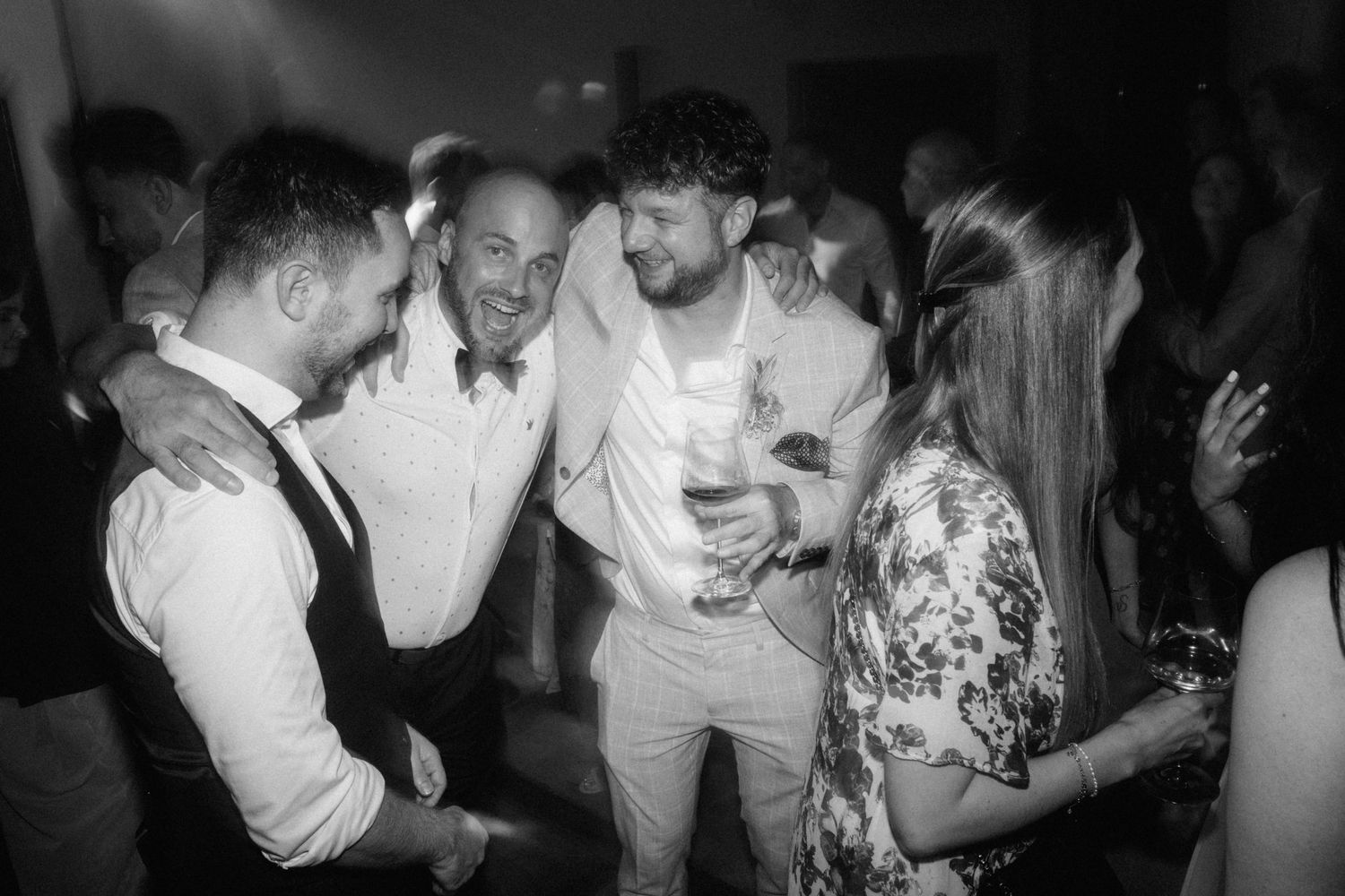 Guests dancing and celebrating joyfully at elegant wedding reception party in black and white photography.