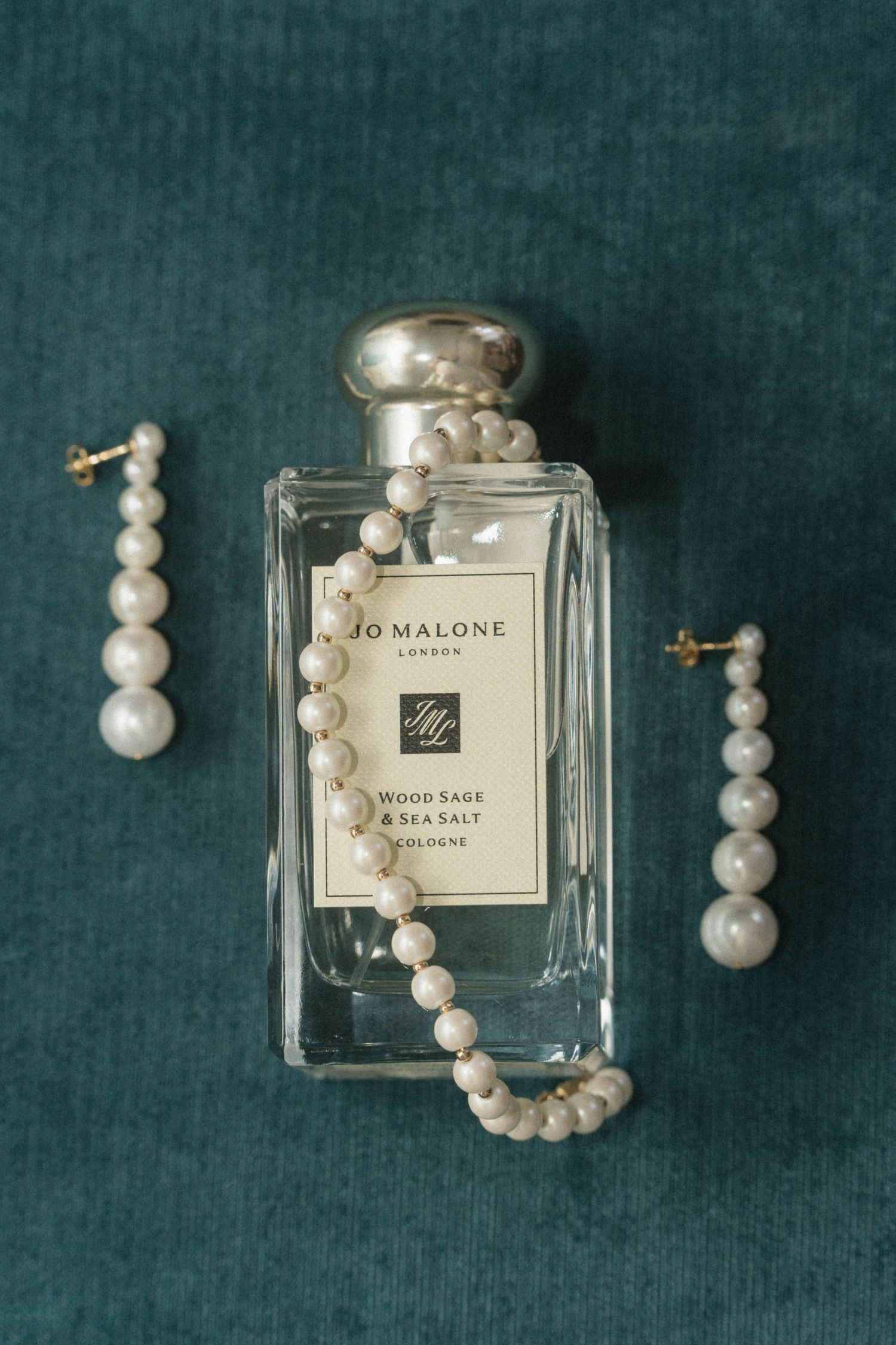 Jo Malone Wood Sage & Sea Salt cologne bottle with pearl necklace and drop earrings on teal velvet.