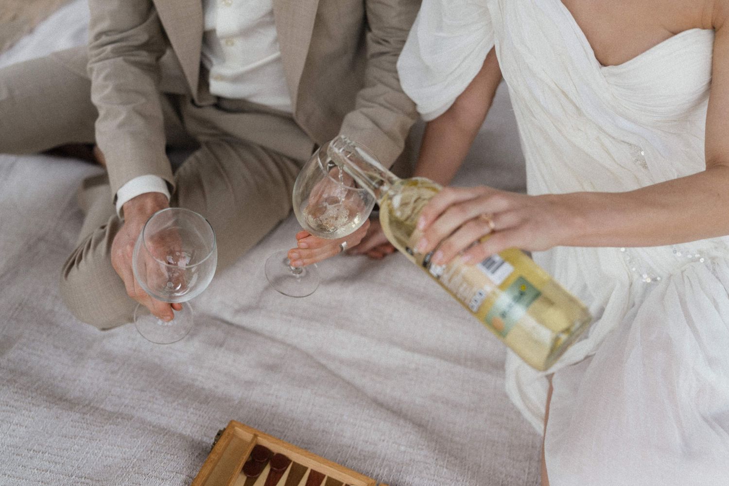 Bride and groom sharing wine during an outdoor wedding picnic celebration.
