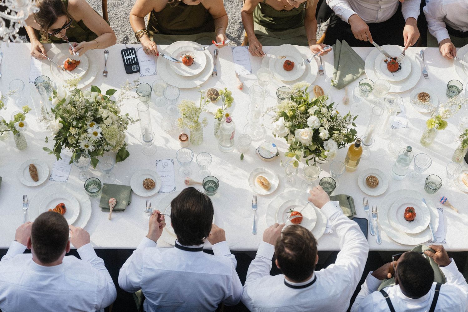 Overhead view of wedding guests dining at elegantly set rectangular table with white floral centerpieces.