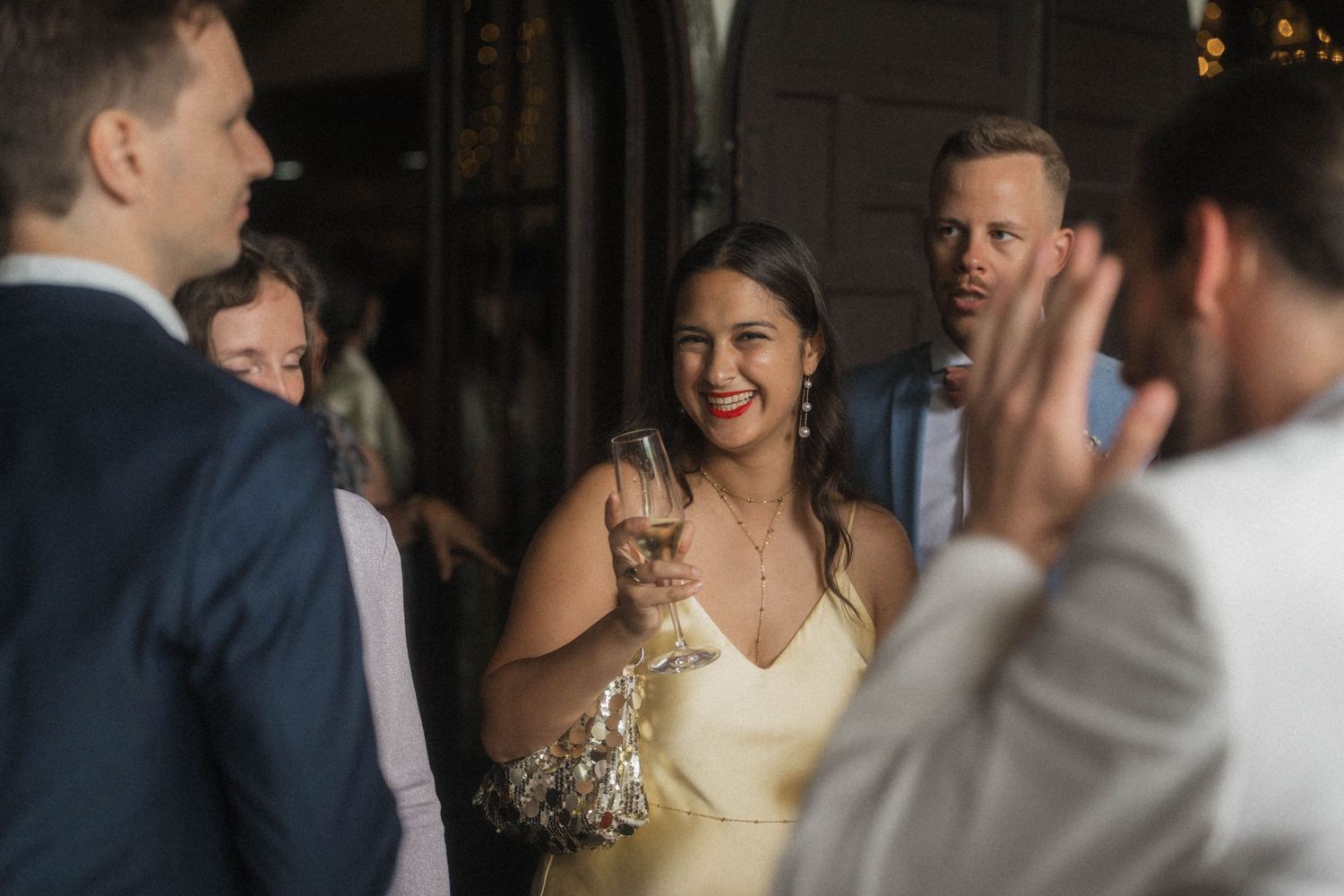 Smiling woman in yellow dress toasting with champagne glass at elegant wedding reception.