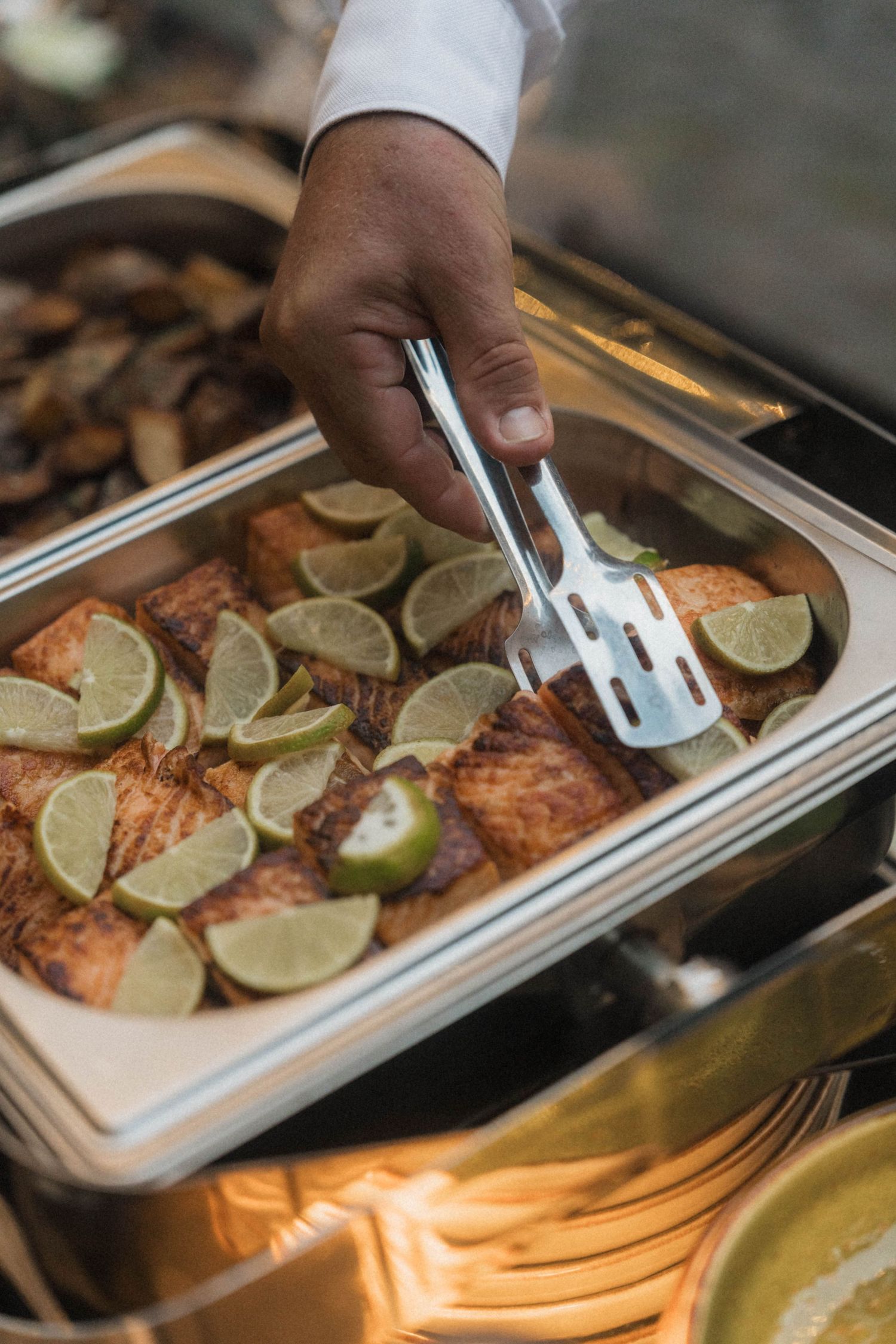 Catering staff serves baked salmon topped with lime slices at a wedding reception buffet.