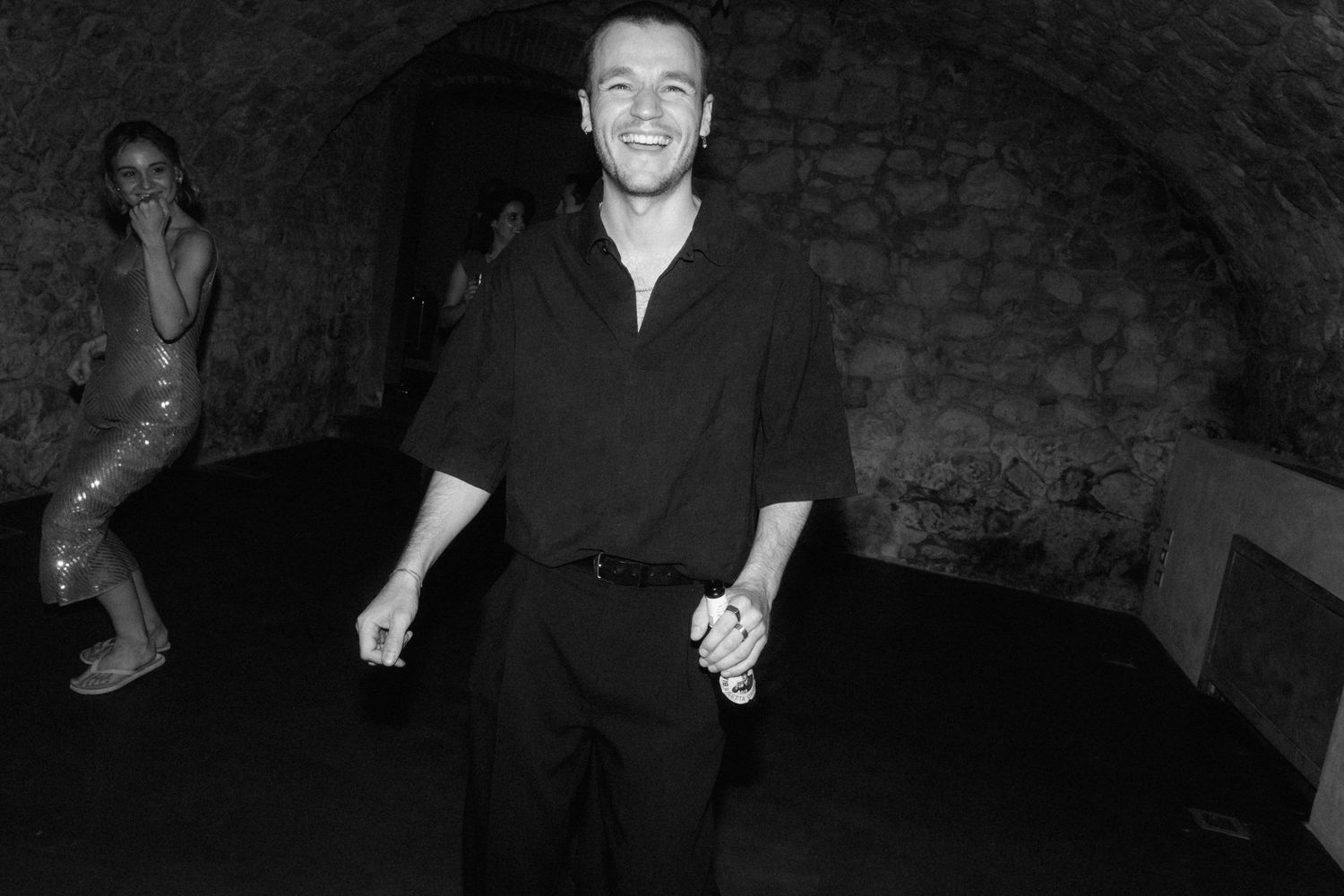 Man smiling and dancing in a stone-walled venue at a black and white party event.
