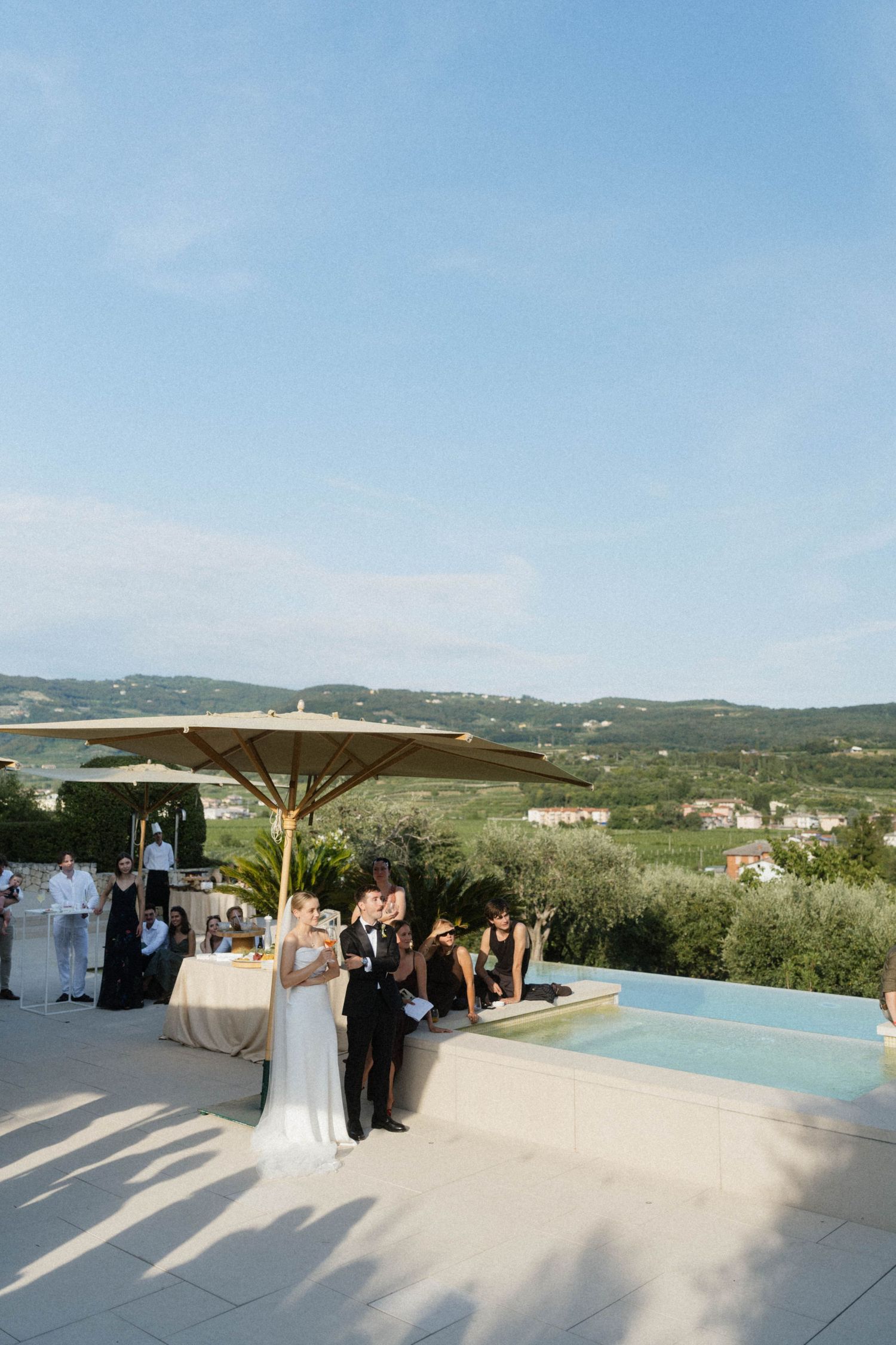 Bride and groom celebrate with guests at an outdoor Italian villa wedding reception beside a stunning infinity pool.