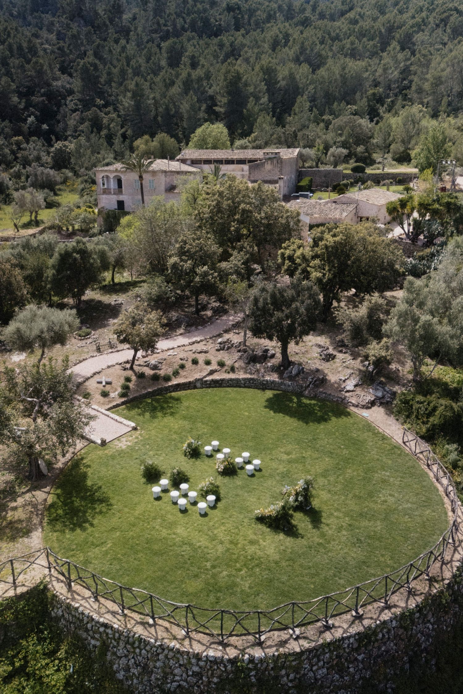 Aerial view of a circular garden with white chairs set up for an outdoor wedding ceremony at a rustic estate.