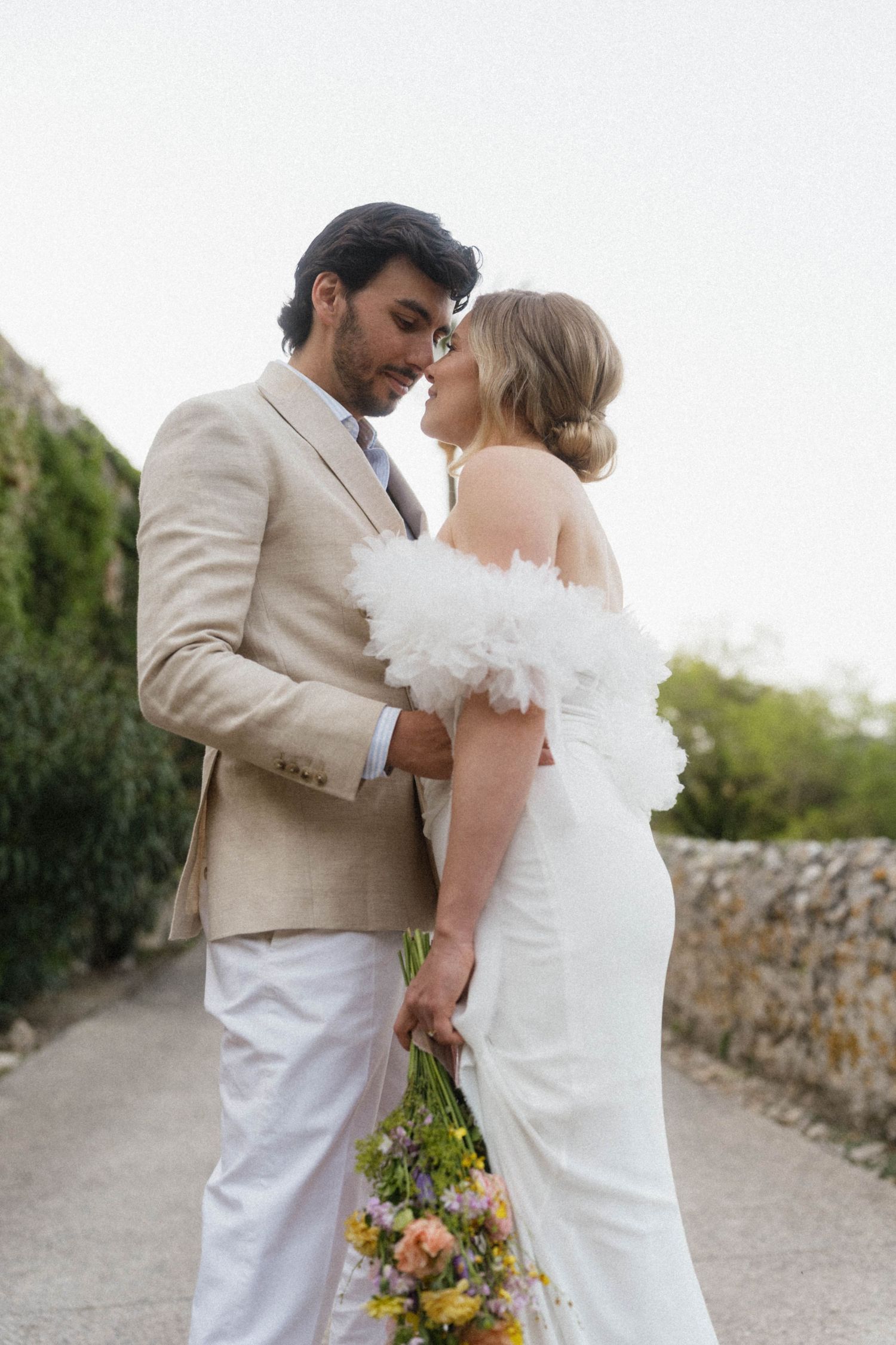 Bride and groom sharing romantic moment on garden path, bride holding colorful wildflower bouquet.