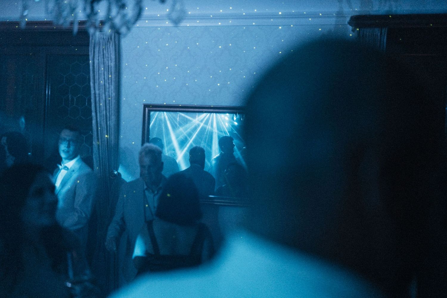 Wedding guests dancing under blue lights and laser beams at evening reception party.