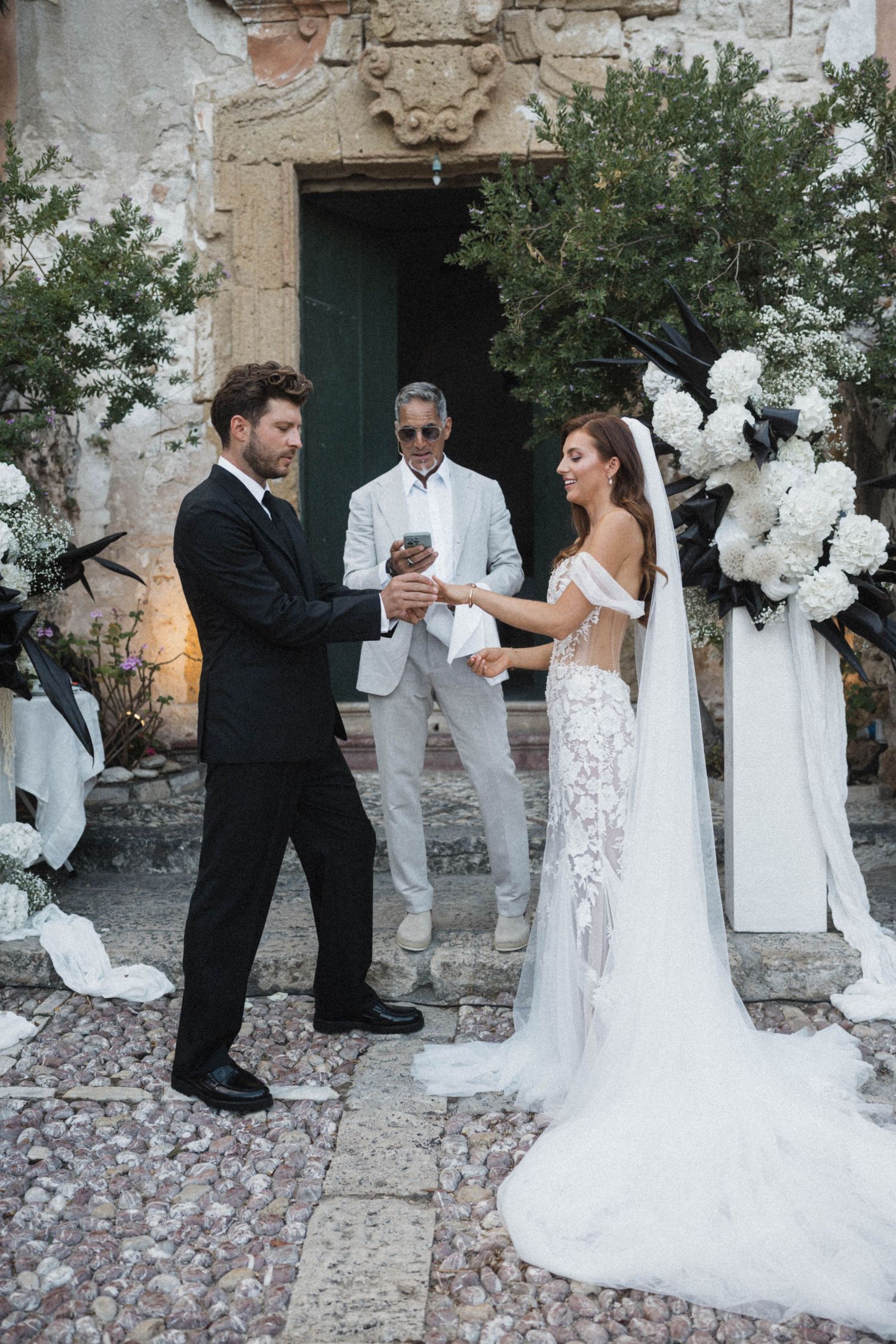 Bride and groom exchange vows before officiant at rustic outdoor wedding ceremony.
