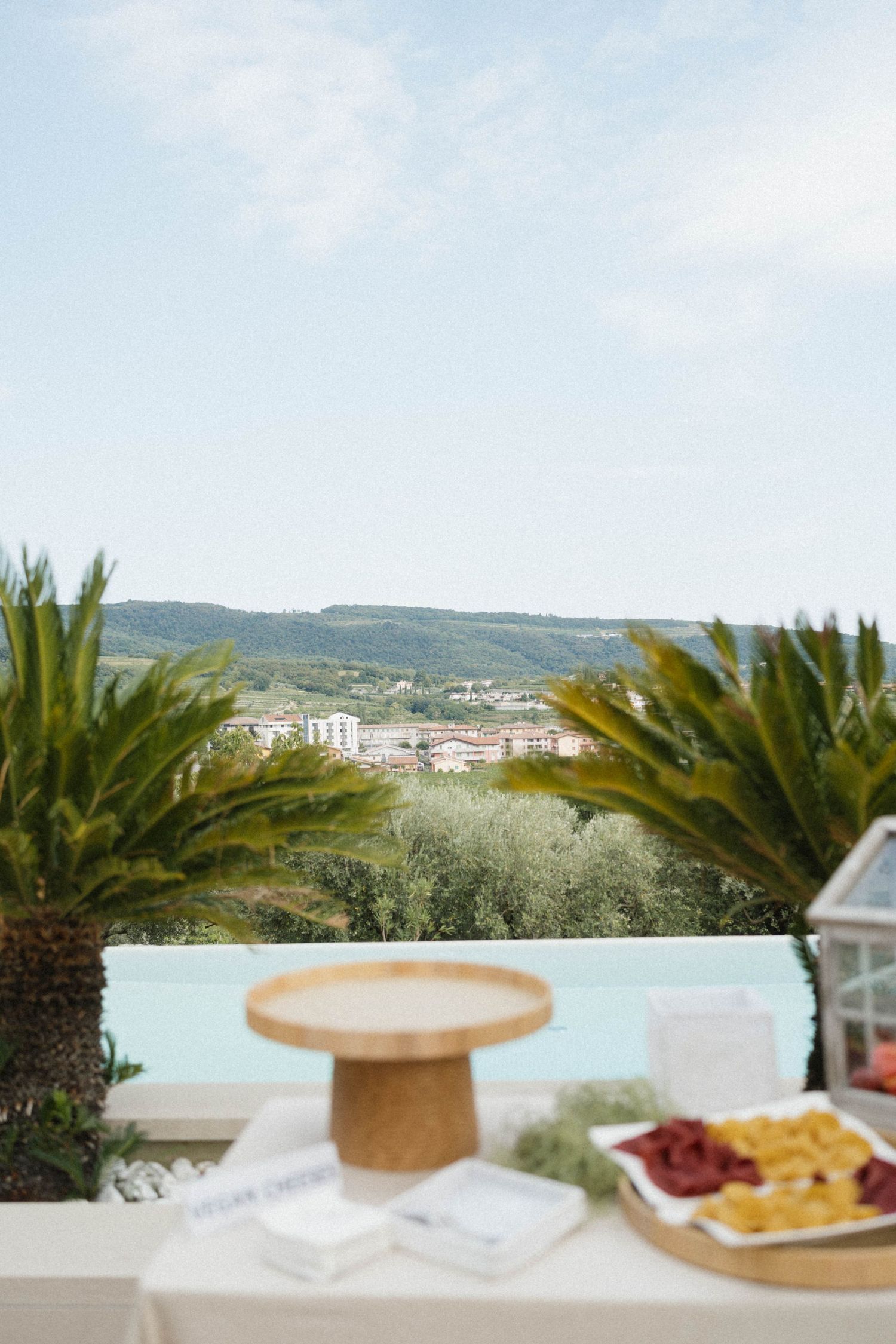 Elegant outdoor wedding reception table with charcuterie spread, overlooking an infinity pool and lush Italian hillside landscape.
