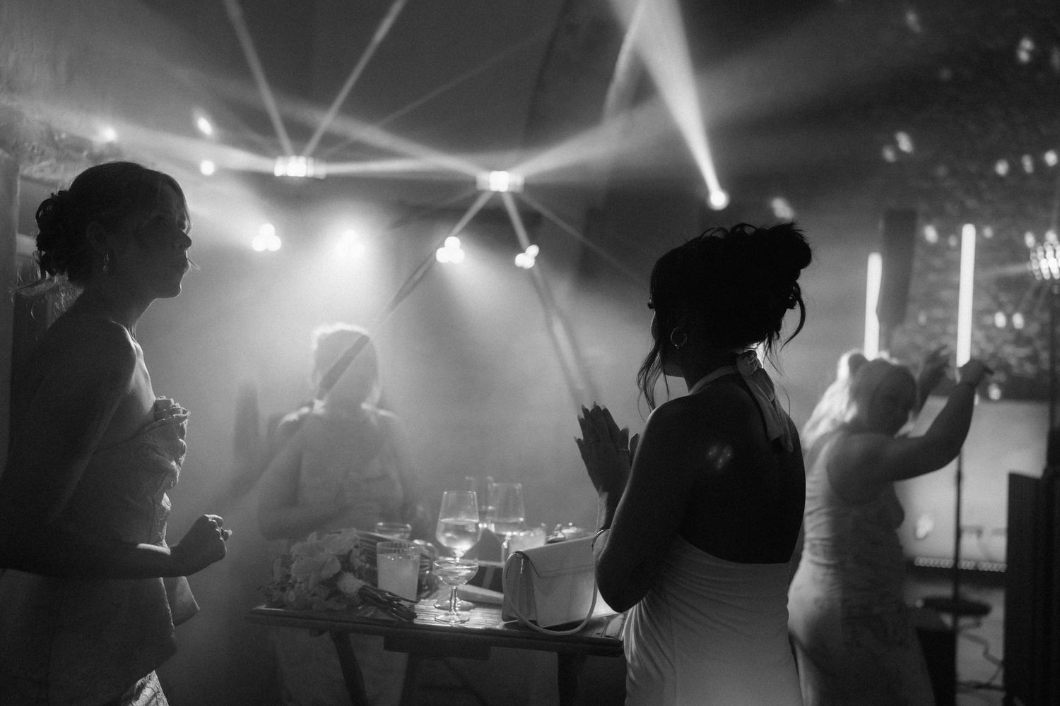 Black and white photo of women dancing at a wedding reception with dramatic stage lighting and fog effects.