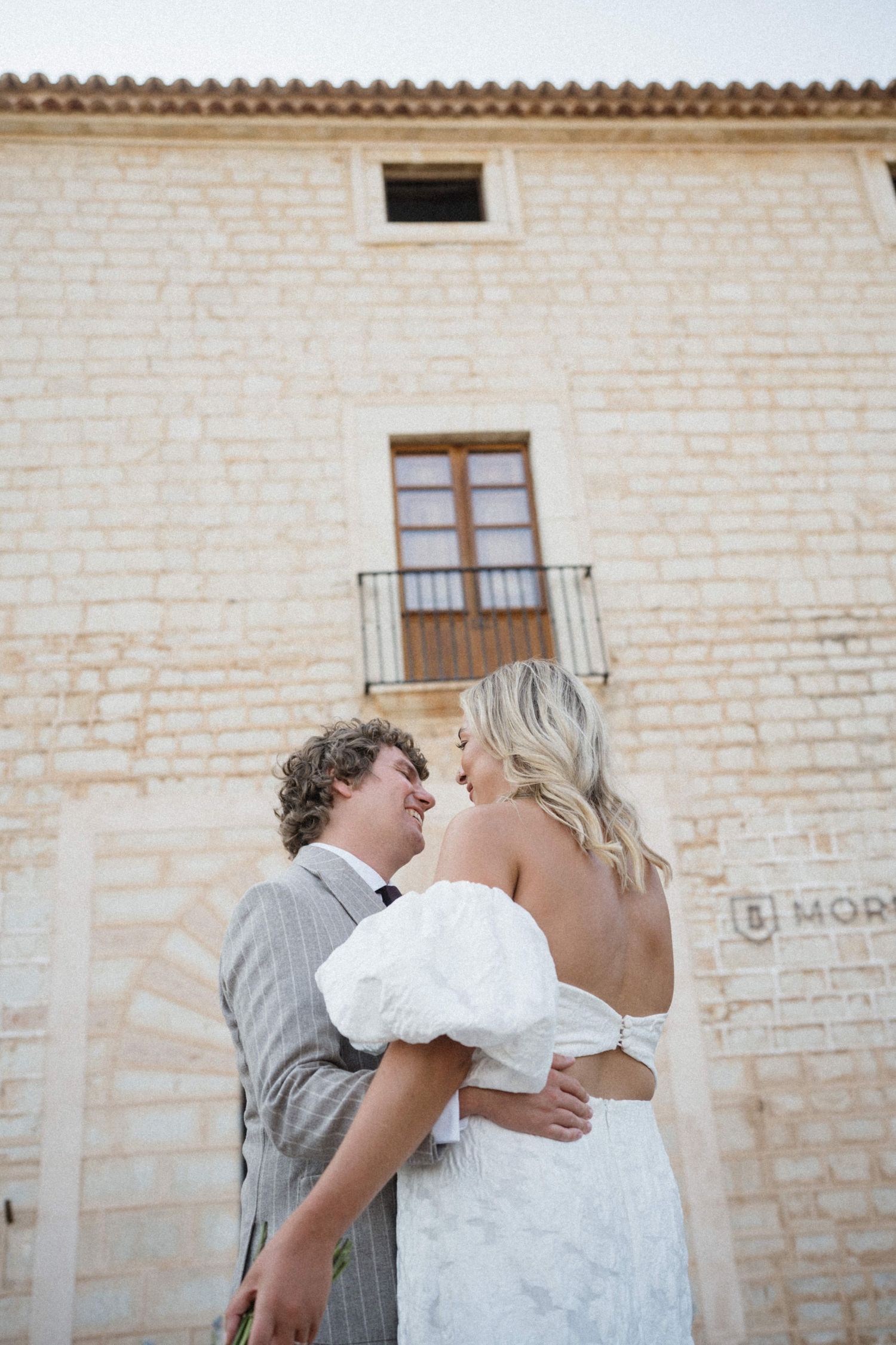 Bride and groom smiling at each other in front of a rustic stone building at Morneta.