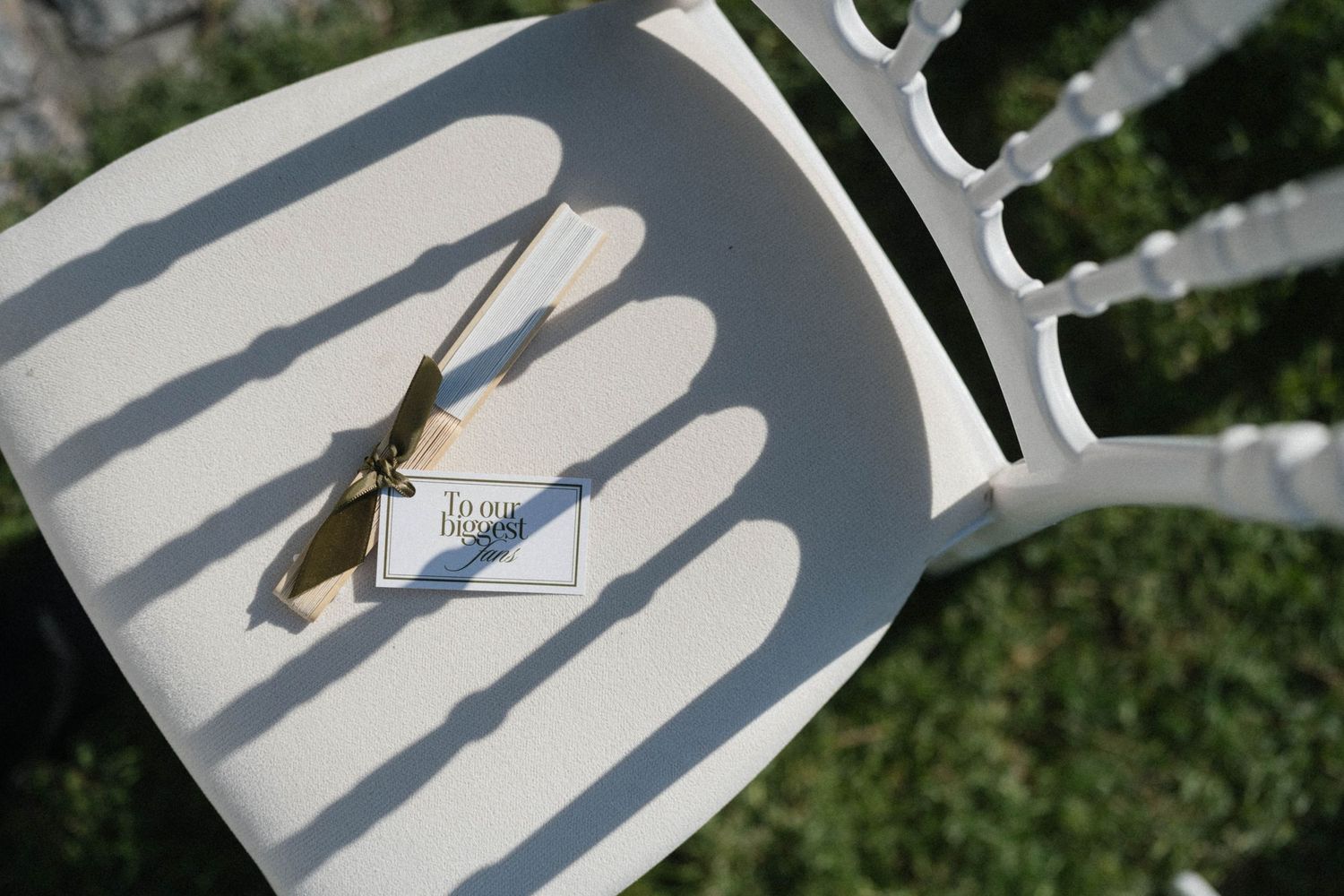 A praying mantis rests on a white decorative chair casting shadows in bright sunlight outdoors.