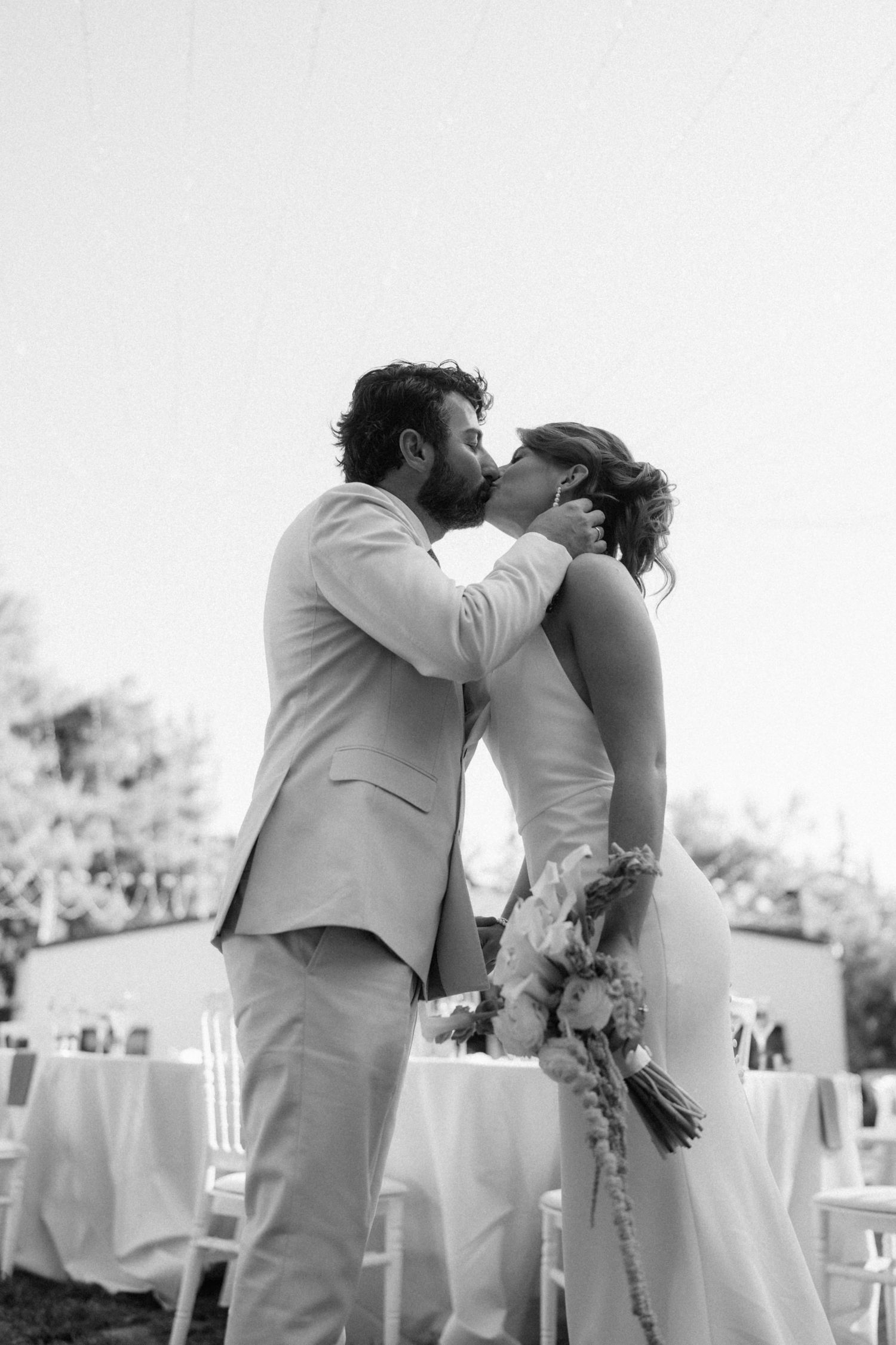 Black and white photo of a bride and groom sharing their first kiss at an outdoor wedding ceremony.