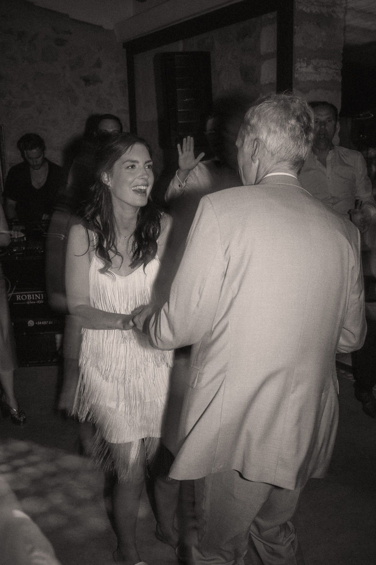 Black and white photo of a woman in a fringed dress dancing with an older man in a suit at a party.