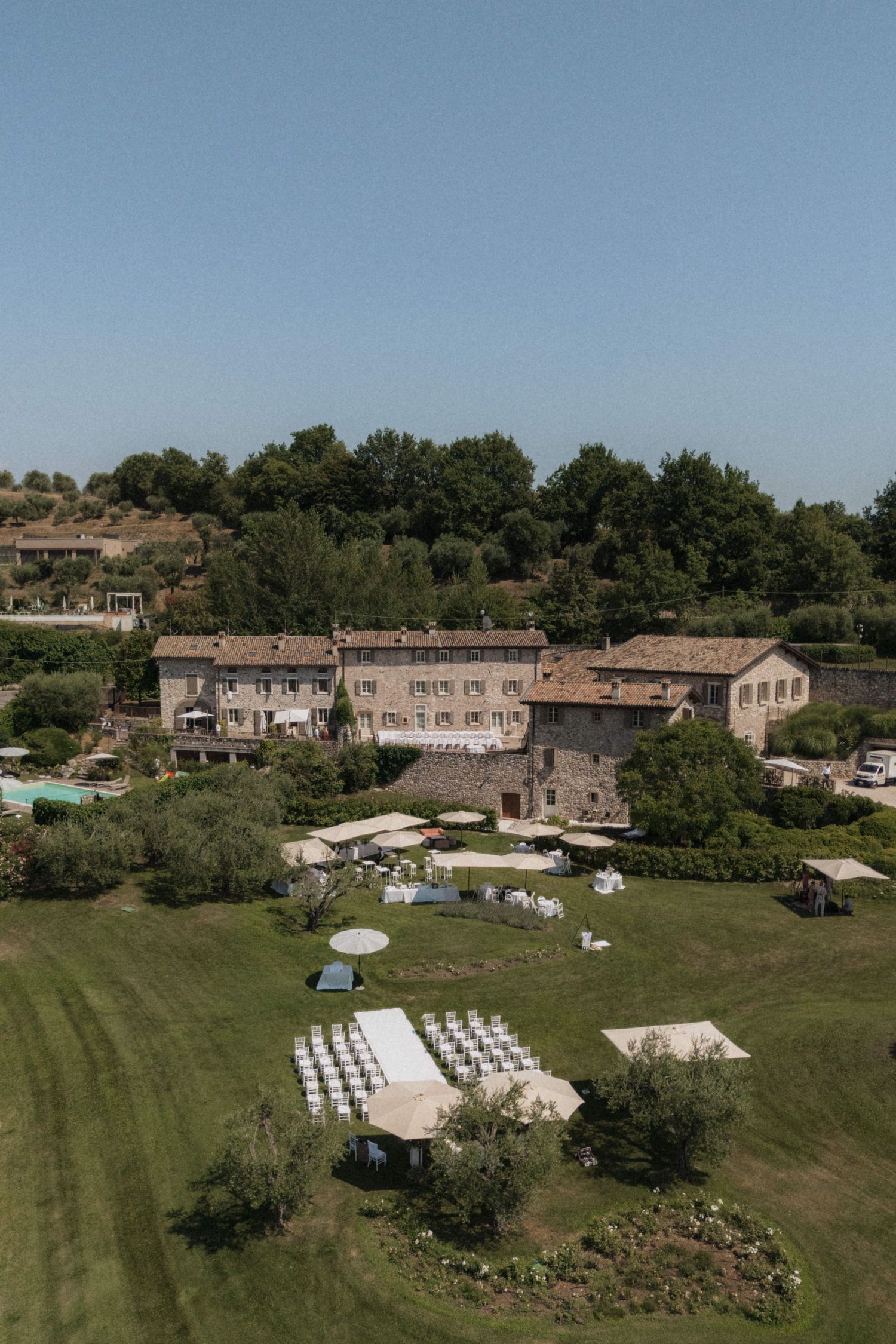 Aerial view of rustic Italian villa wedding venue with white chairs arranged on green lawn.